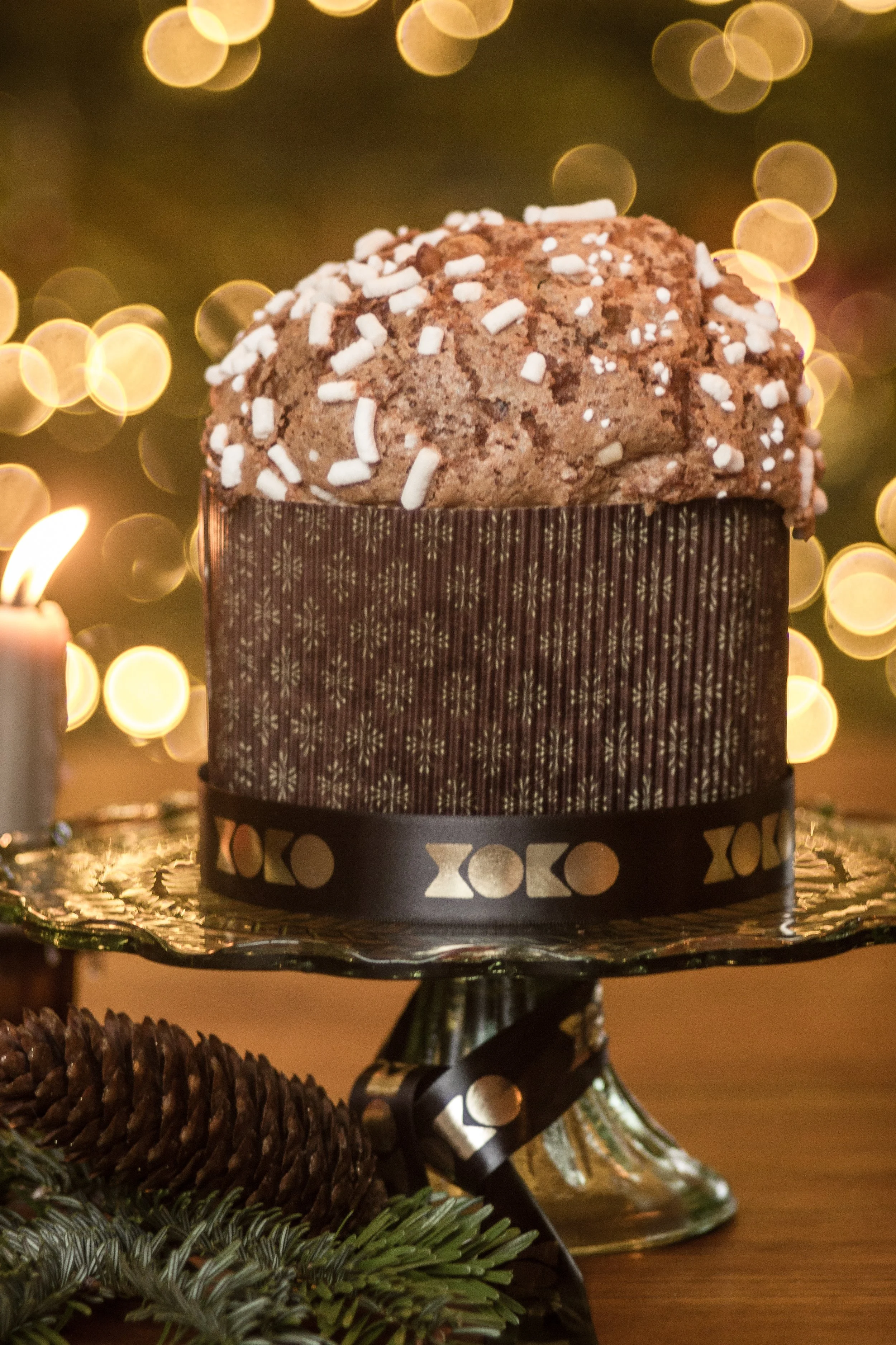 Handcrafted artisan sourdough panettone topped with pearl sugar on an ornate stand, wrapped with a branded XOKO ribbon in a festive holiday setting.