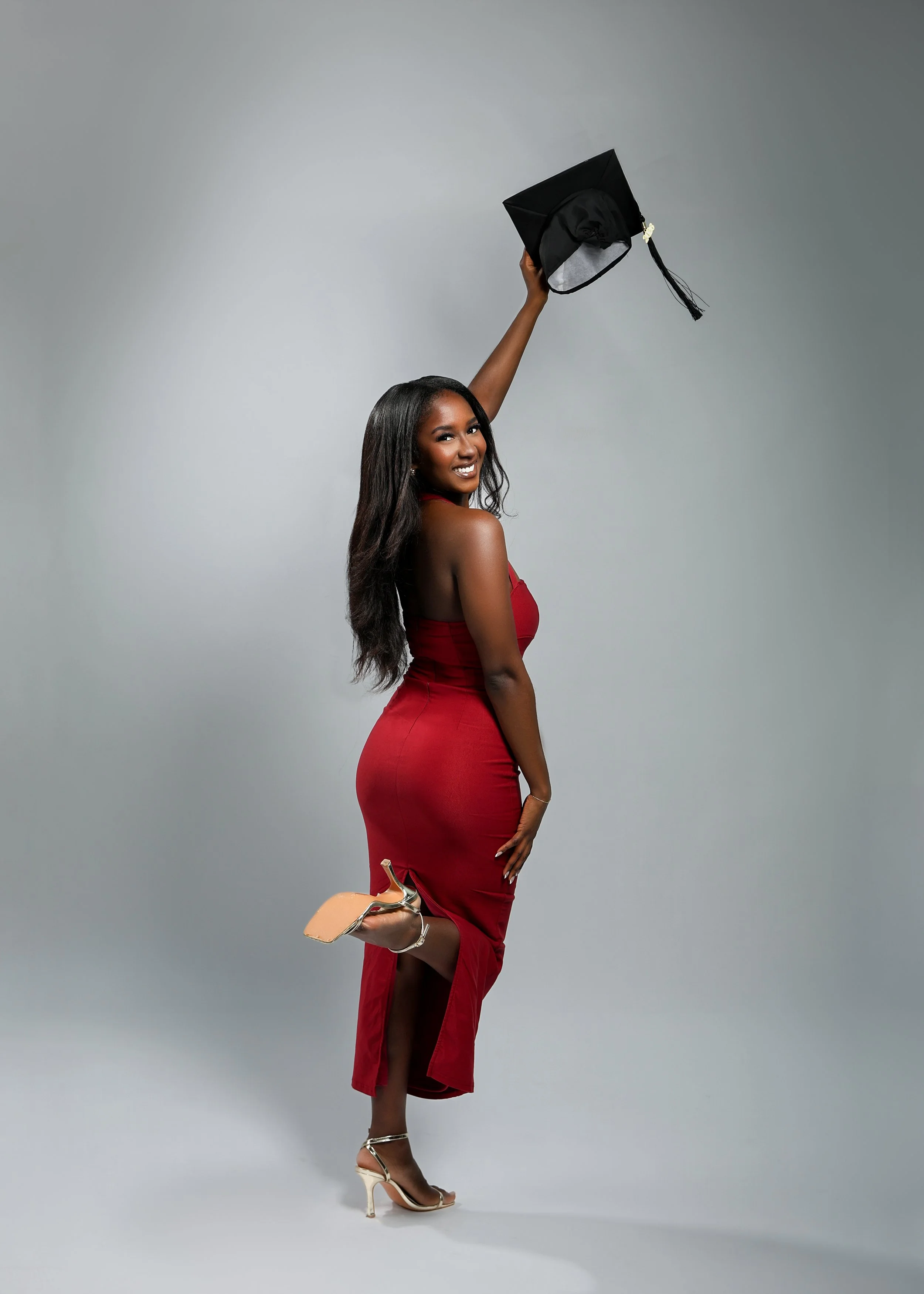 grad photo of woman in red dress holding up her graduation cap