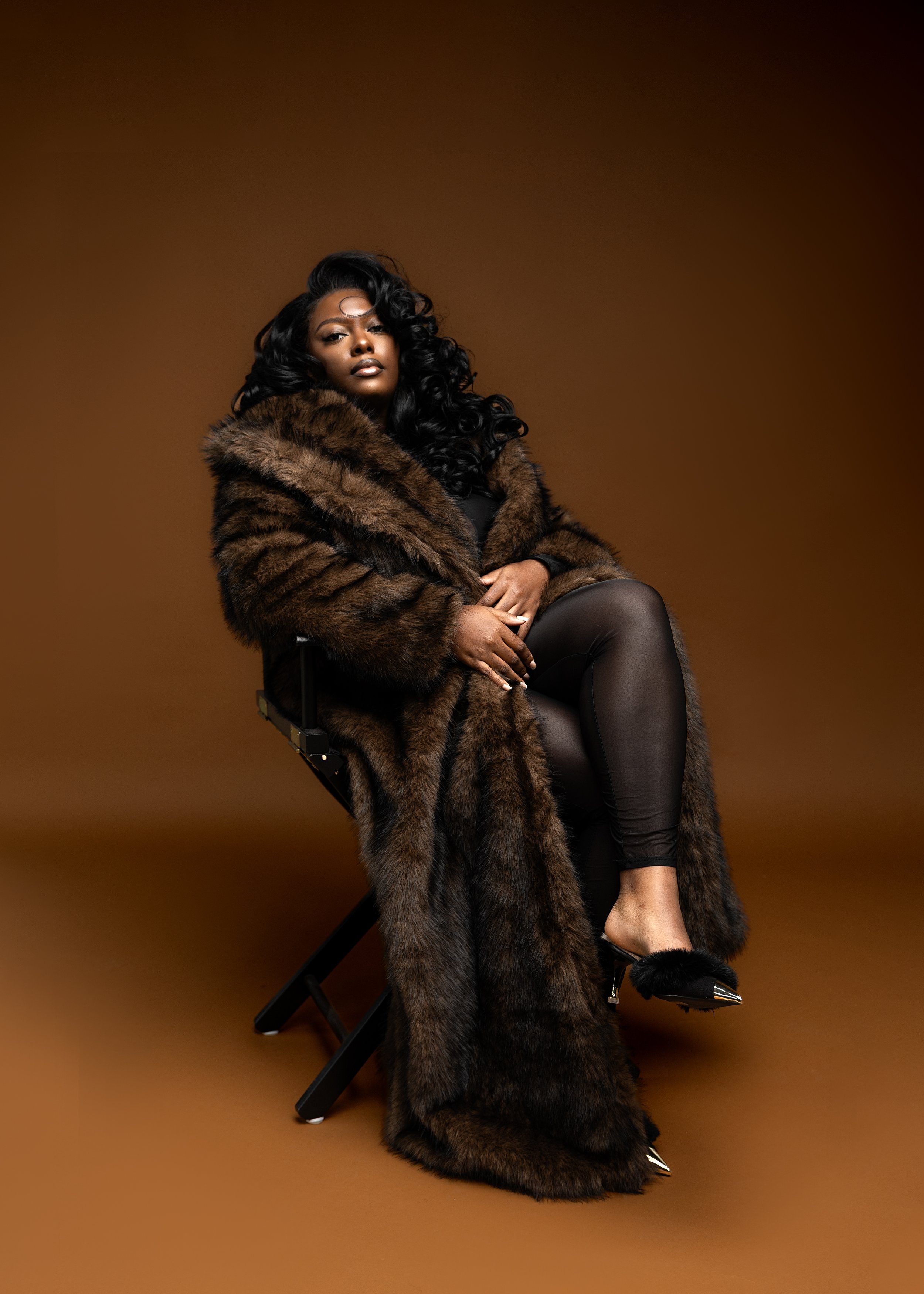 A woman with curly hair in a gold and pearl decorated dress poses against a orange background.