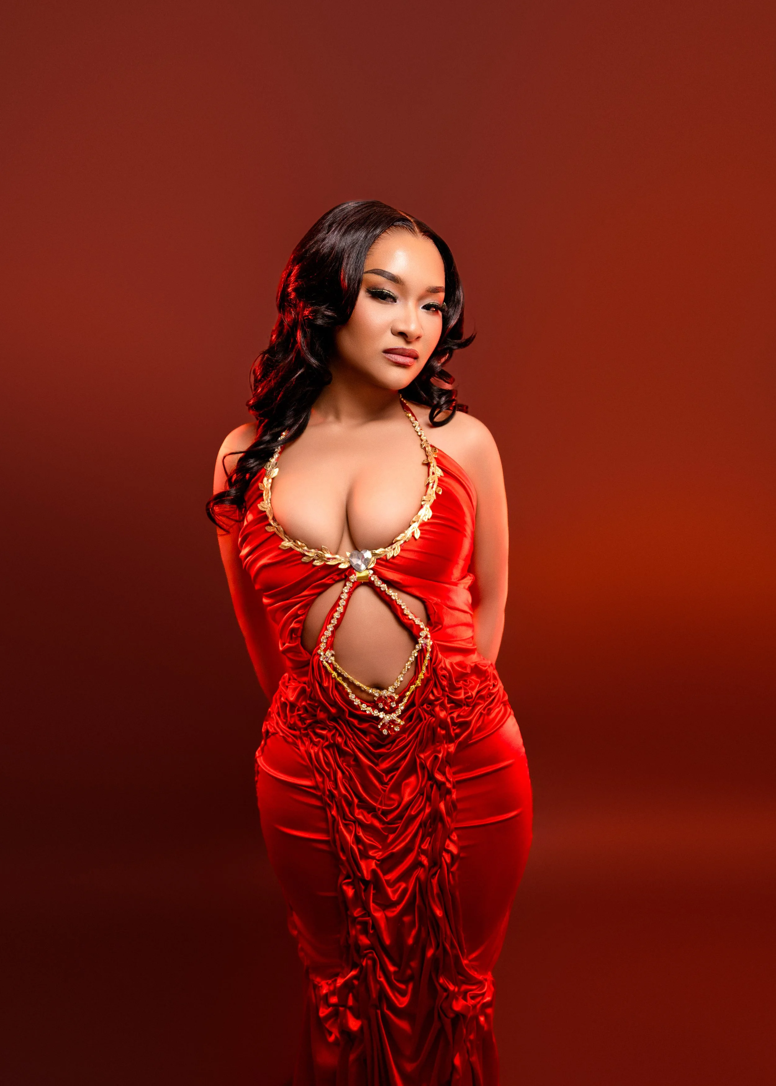 A woman wearing a revealing red dress with gold embellishments poses against a red background.