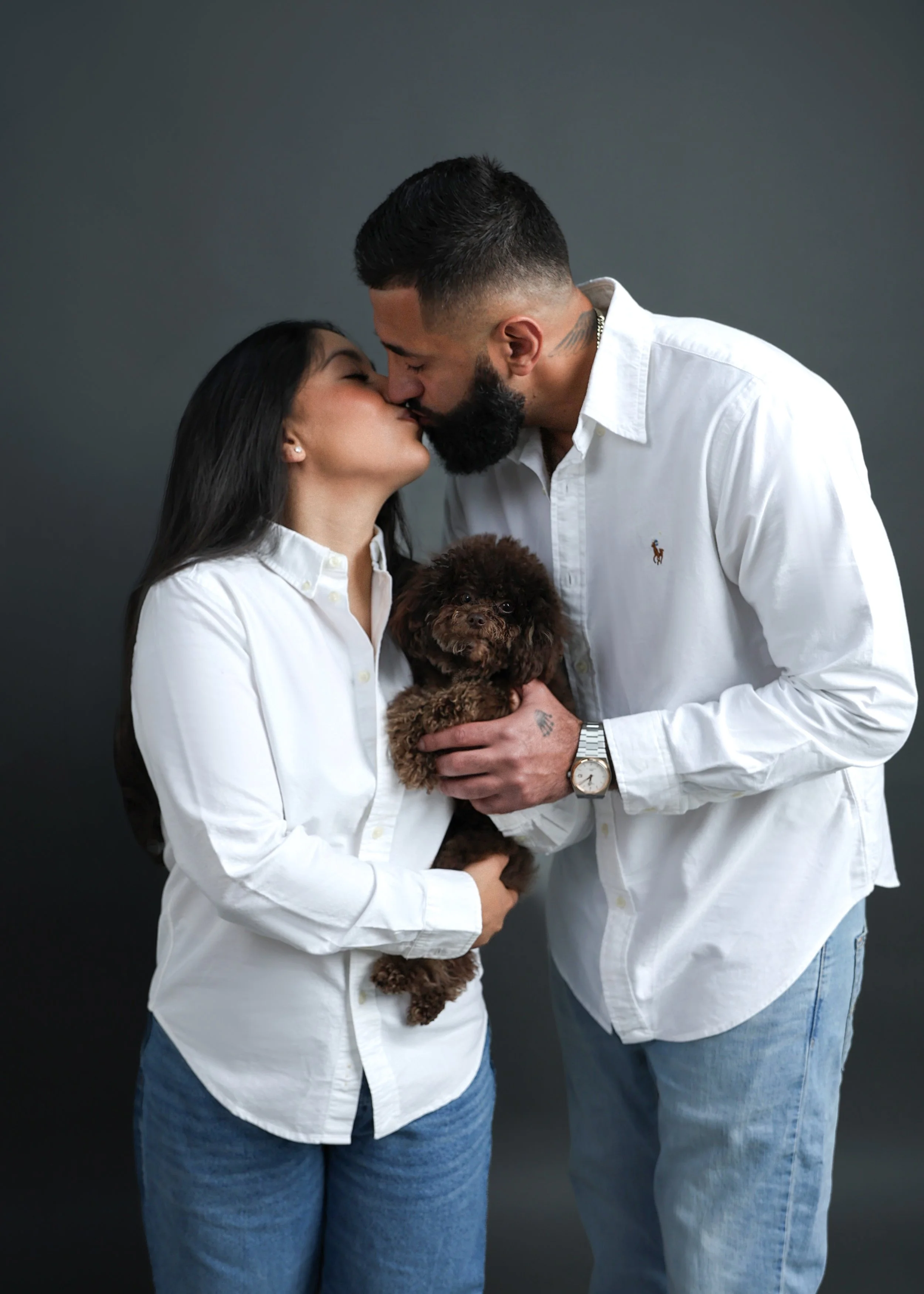 family photo of Couple kissing while holding their dog