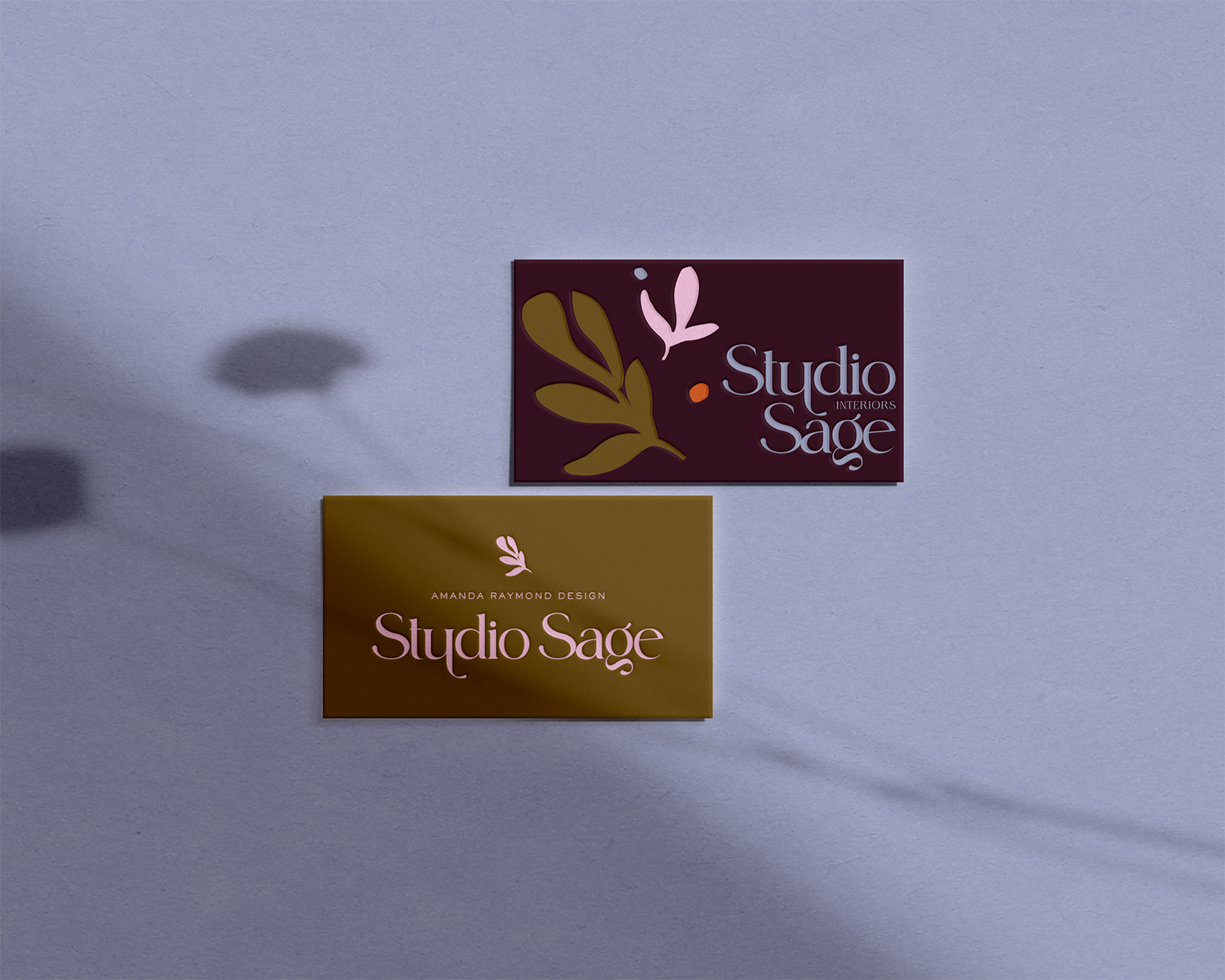 Two business cards on a purple surface, one dark red and the other mustard yellow, both featuring the text 'Studio Sâge' with decorative leaves.