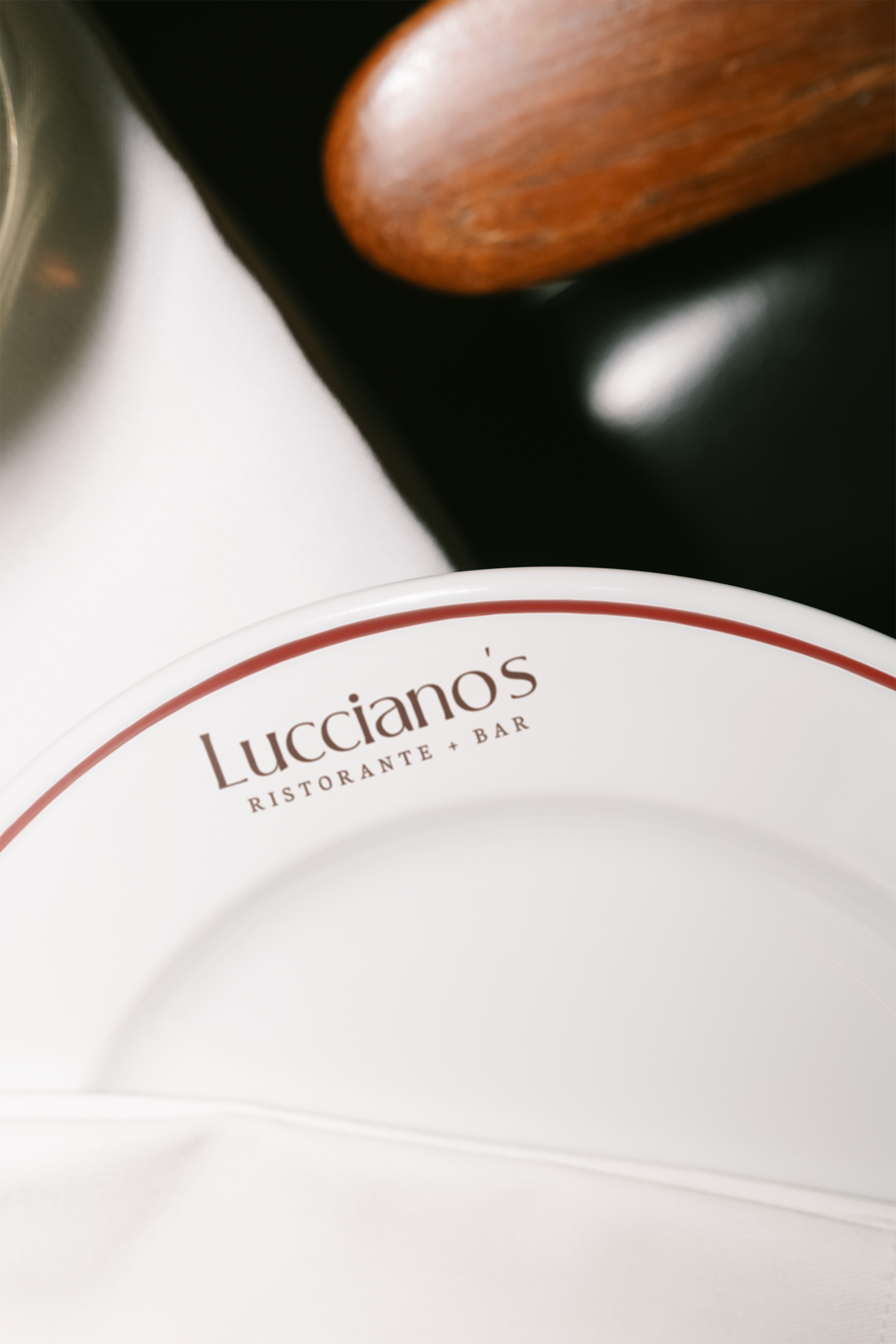 Close-up of a white plate with a brown restaurant logo, with a wooden object, part of some black and white surfaces in the background.
