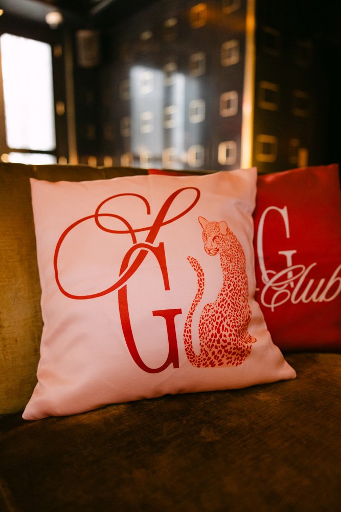 Decorative pillow with red letters and a leopard illustration, placed on a dark wooden surface in a dimly lit environment.