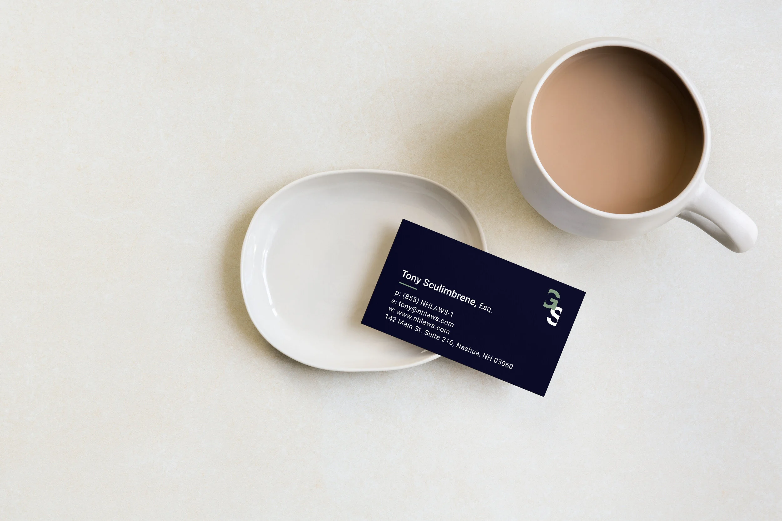 Business card on a saucer next to a cup of coffee on a light surface.