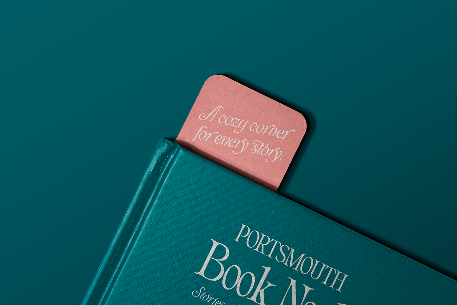 A teal hardcover book titled 'Portsmouth Book N' with a pink bookmark that says 'A cozy corner for every story' tucked inside.