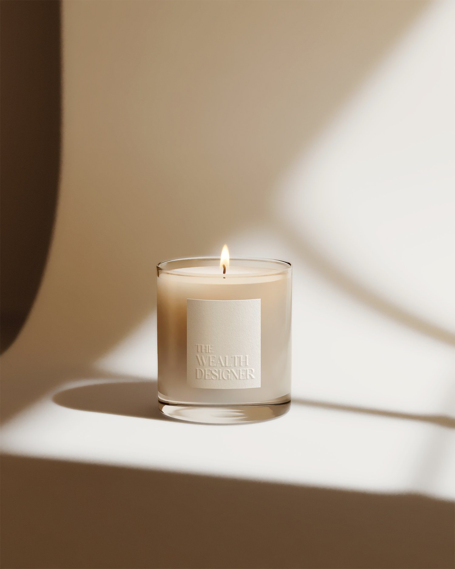 A lit white candle in a clear glass holder with a white label that reads "The Wealth Designer." The background is neutral and softly lit, creating a calm and minimalist aesthetic.