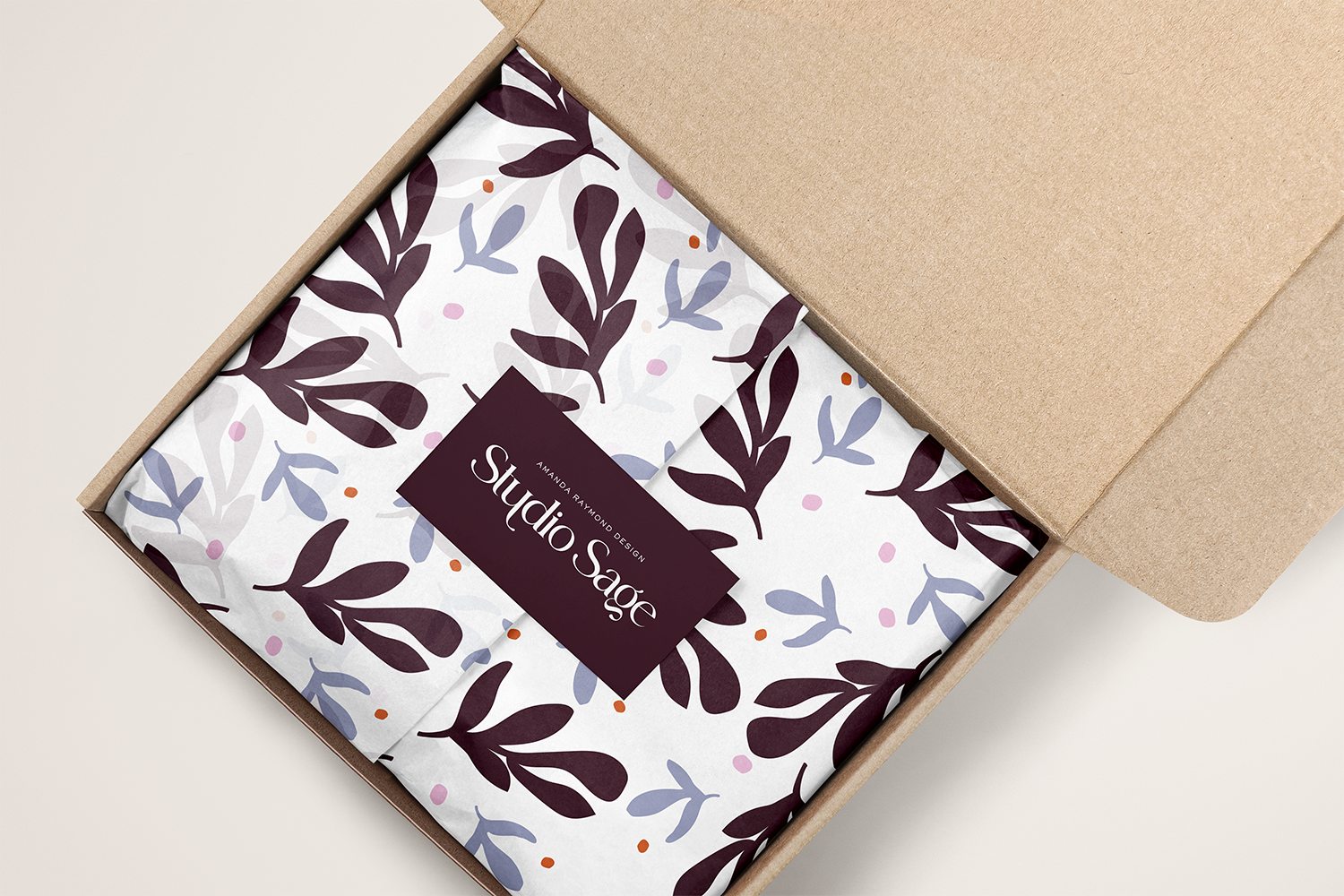 Unopened cardboard box containing wrapped gift with floral patterned paper and a label that reads 'Studio Sage' by Amanda Raymond Design.