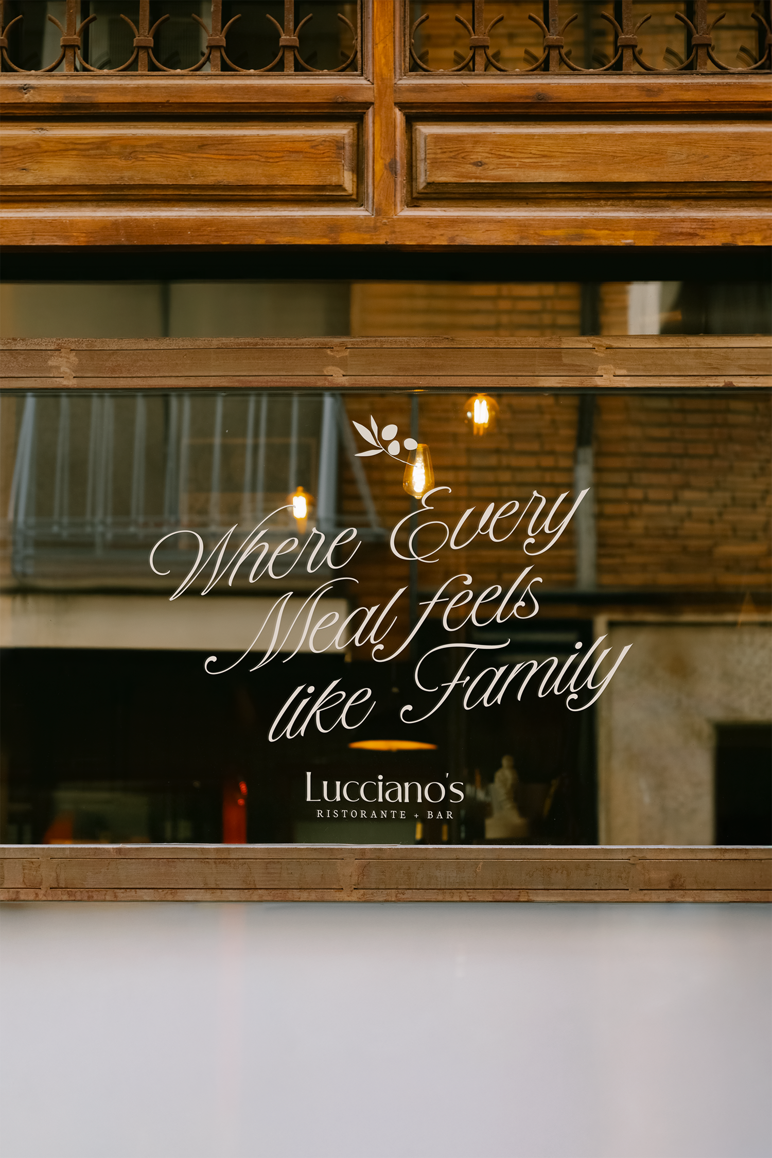 Reflection of a wooden window frame with a quote that says, 'Where Every Meal Feels like Family' and the name 'Lucciano's Ristorante + Bar' underneath.