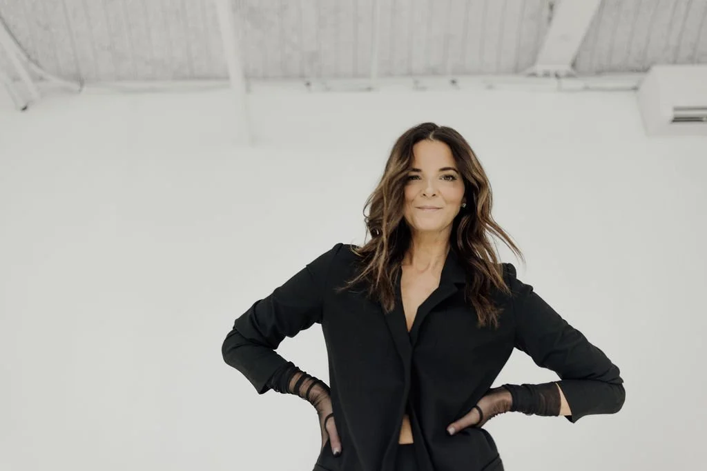 Person wearing a black outfit with long sleeves, standing with hands on hips, against a white background.