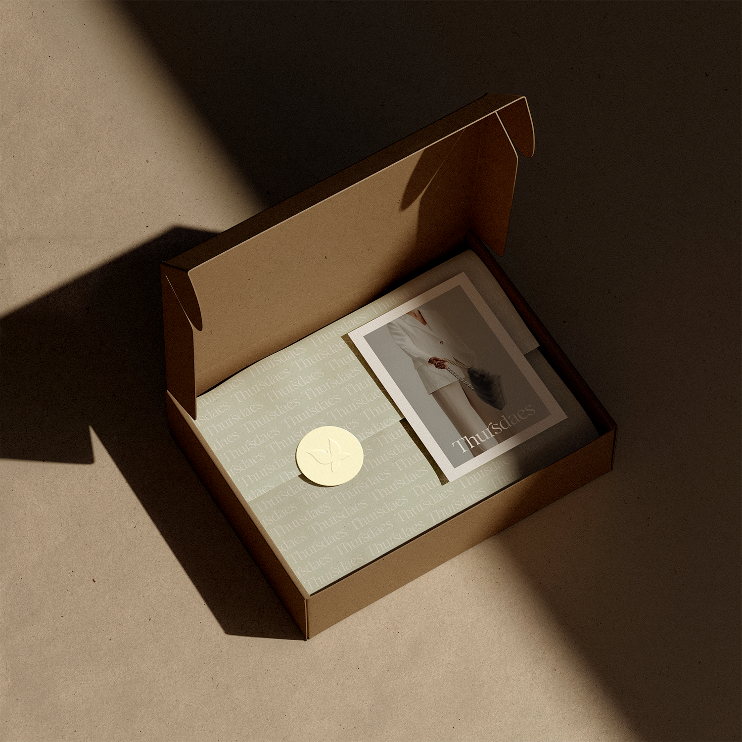 Open cardboard box containing a catalog or brochure with a person in white clothing on the cover, and a round cream-colored sticker with a butterfly logo inside.