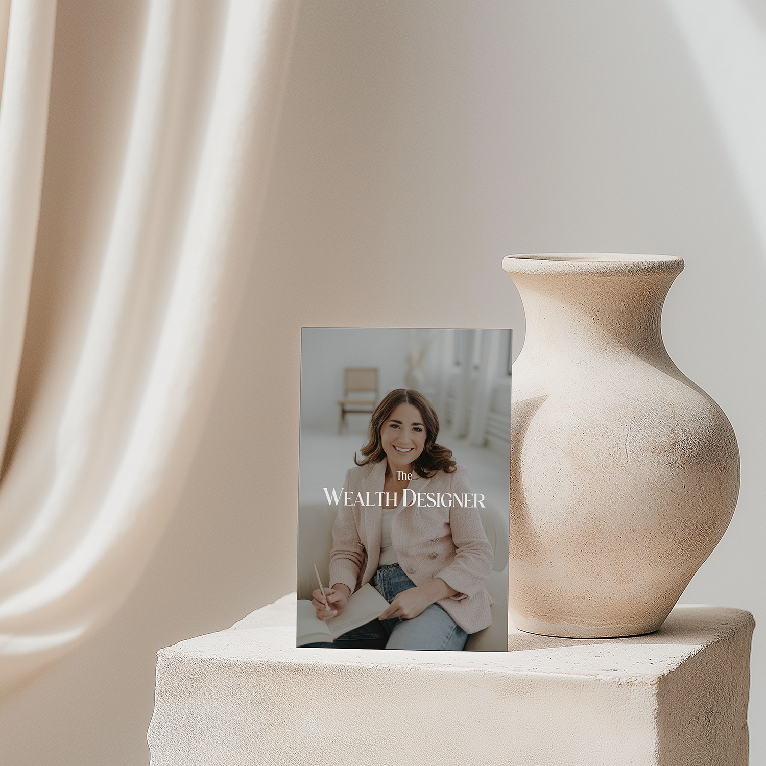 A wooden table with a beige ceramic vase and a book titled "The Wealth Designer" featuring a smiling woman on the cover.