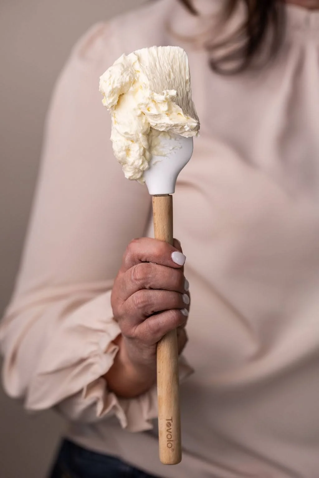 Person holding a wooden-handled spatula with a large scoop of vanilla ice cream.