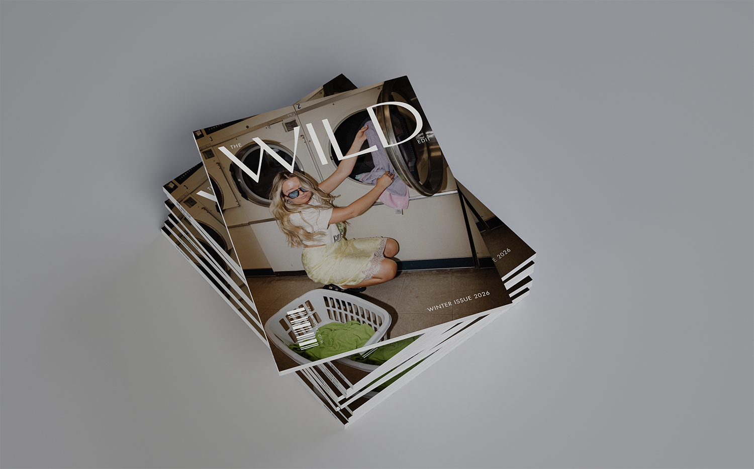 Stack of magazines or brochures, with the top one showing a woman loading laundry into a washer or dryer in a laundromat, wearing glasses, a white top, and a yellow skirt.