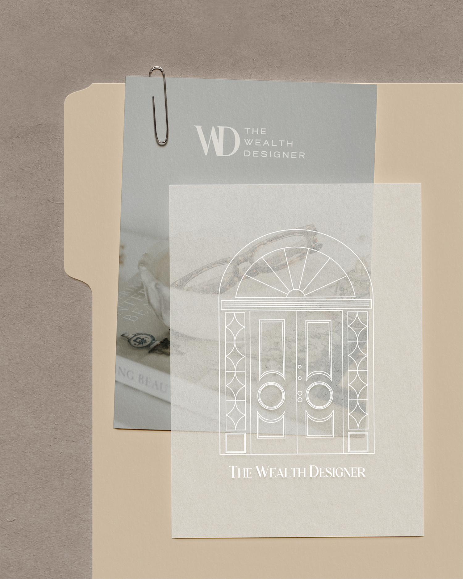 Close-up of a brochure or flyer titled 'The Wealth Designer' with a graphic of a door and decorative design, placed on a beige surface, with a paperclip attached to the top.