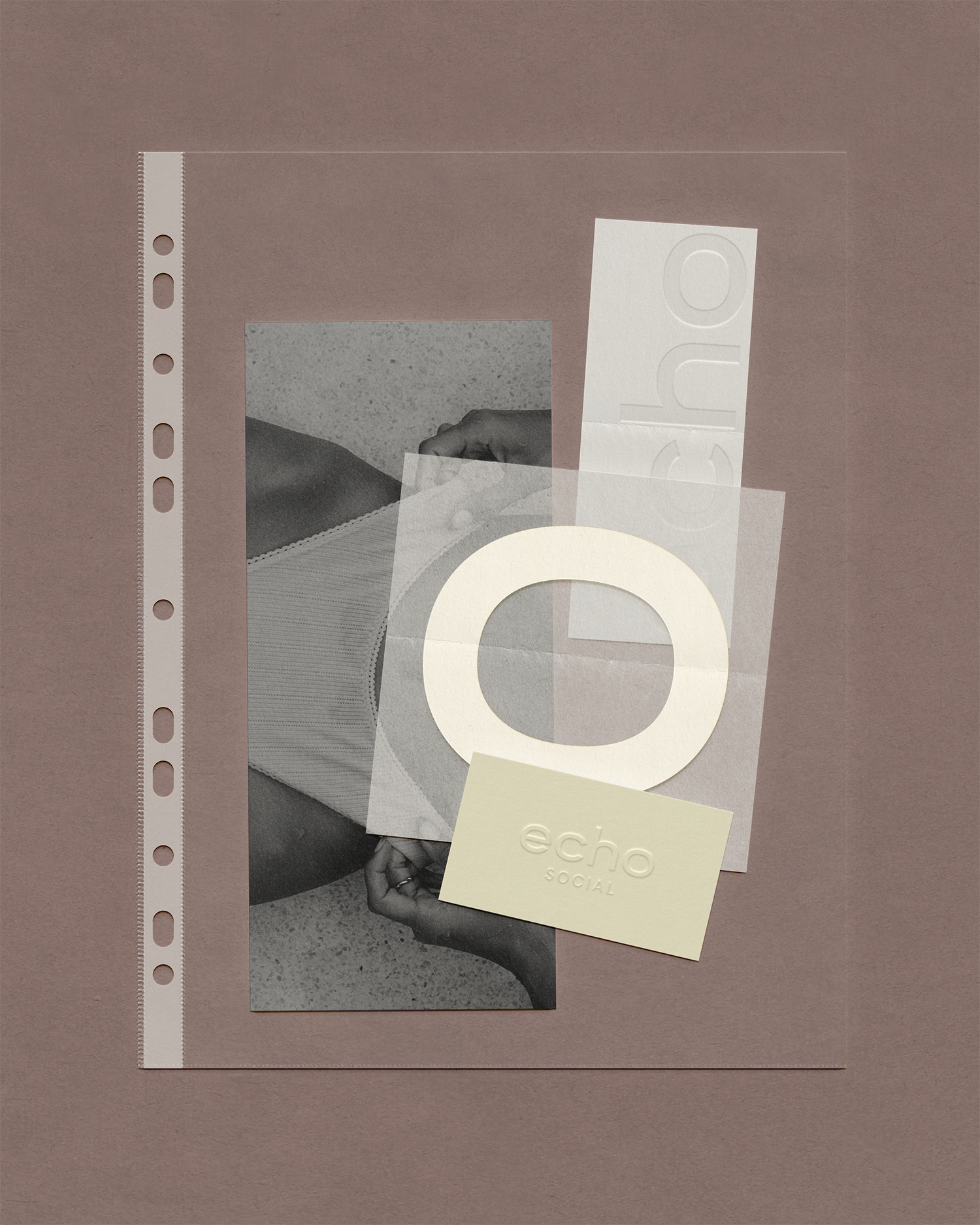 A flat lay of various printed materials including a black and white photograph, a semi-transparent acetate sheet, a white card with embossed text, and a yellow card, all placed on a textured pink background.
