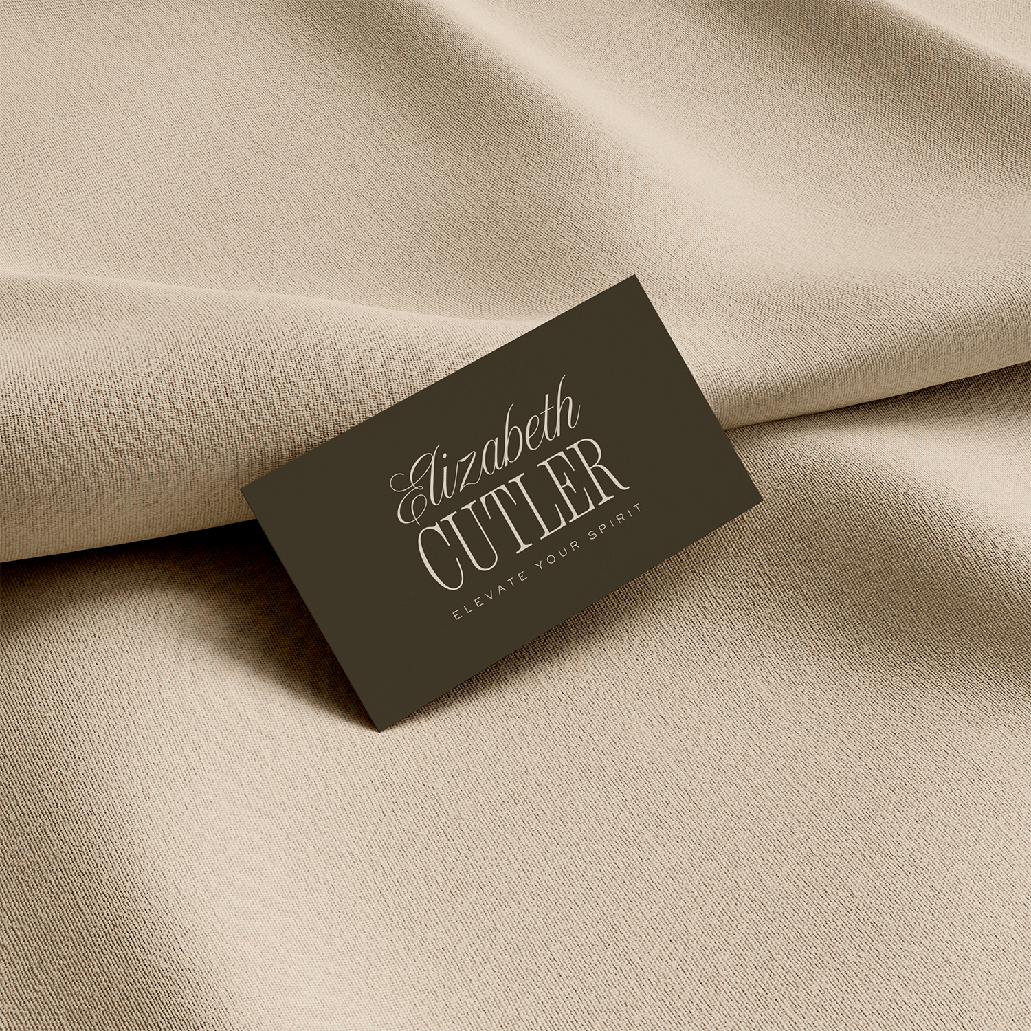 A black business card with white text reading 'Elizabeth Cutler' and 'Elevate Your Spirit' resting on beige fabric.