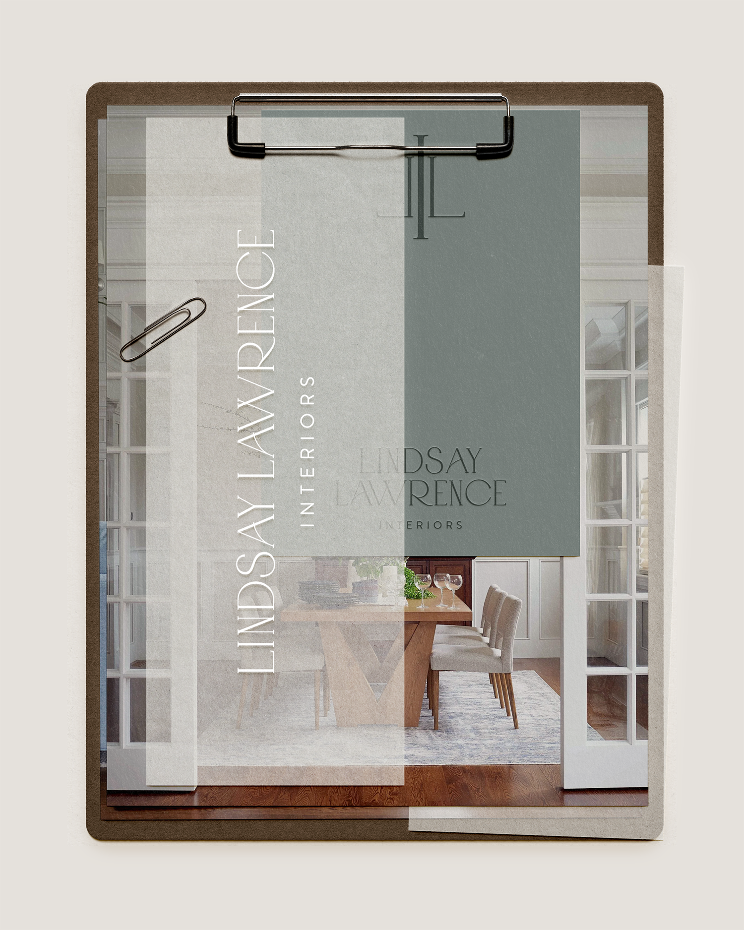 A sign for Lindsay Lawrence Interior Interiors hanging on a door frame, with a dining room visible inside featuring a wooden table, chairs, and a window with white curtains.