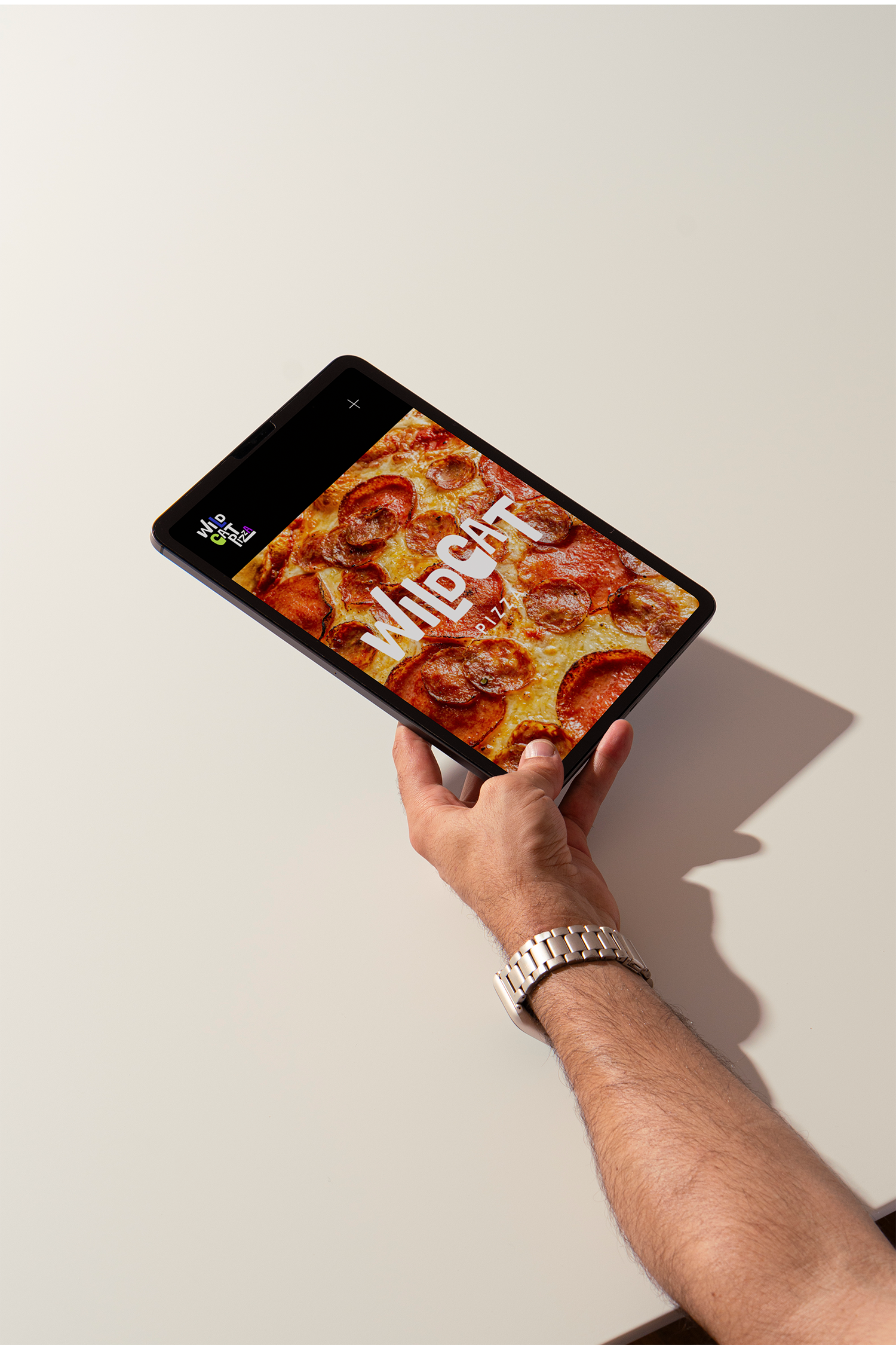 A person holding a smartphone with a picture of a pepperoni pizza on the screen. The person is wearing a silver wristwatch and has a light skin tone and hairy arm. The background is plain white.