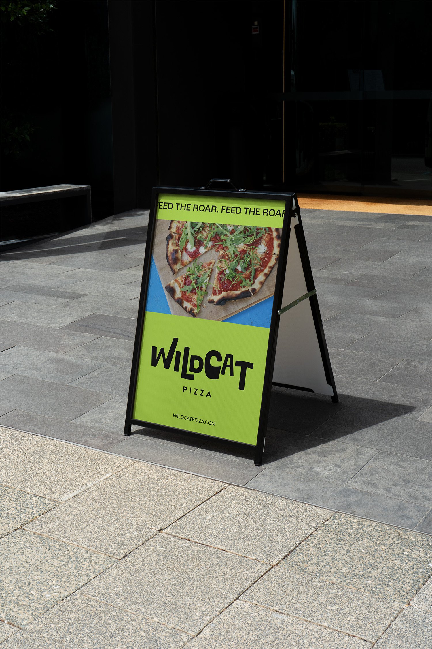 A sidewalk sign advertising Wildcat Pizza with an image of a pizza topped with arugula.