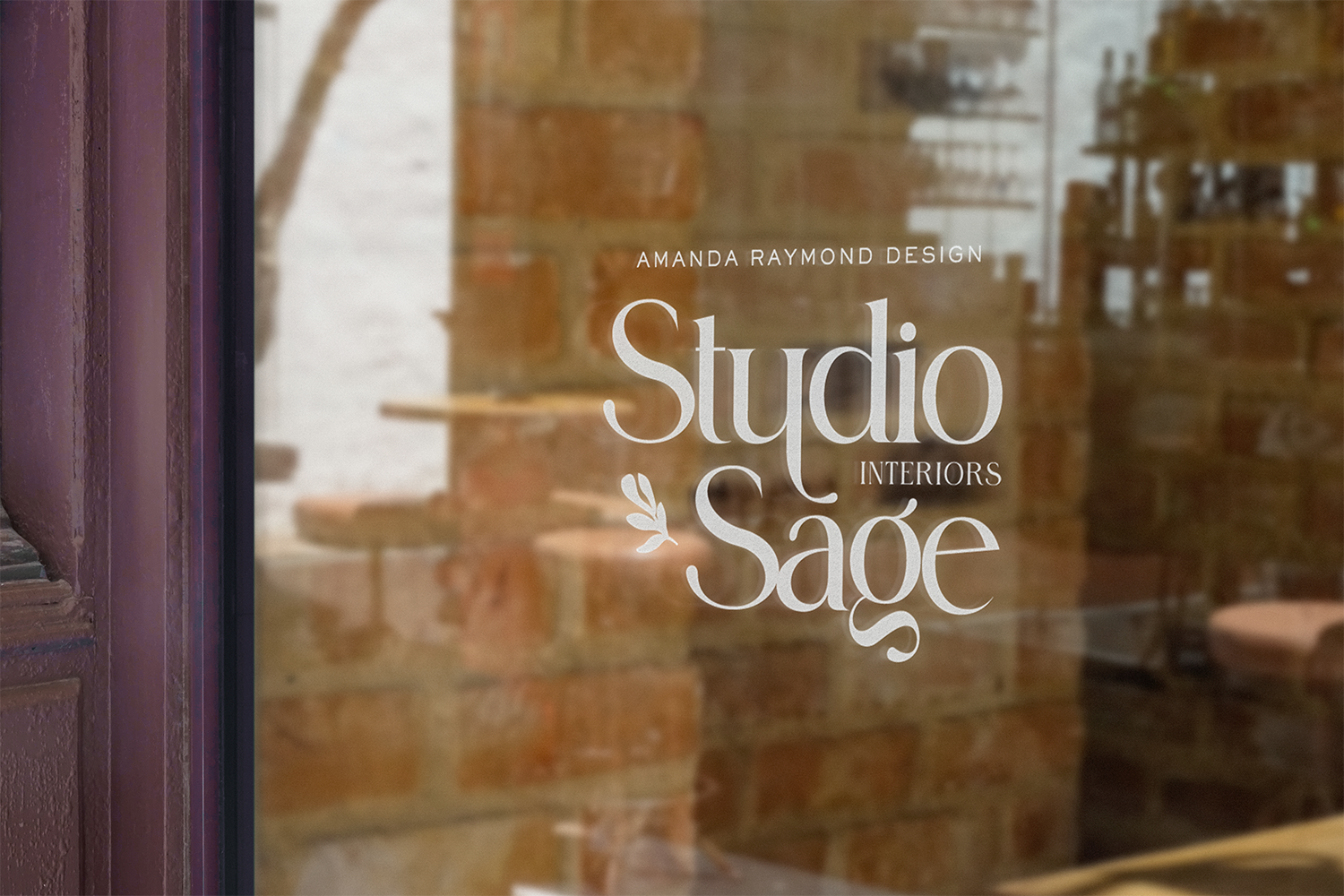 Glass door with printed logo that reads "Studio Sage Interiors" with the names Amanda Raymond Design above and interior images and brick wall reflections in the background.