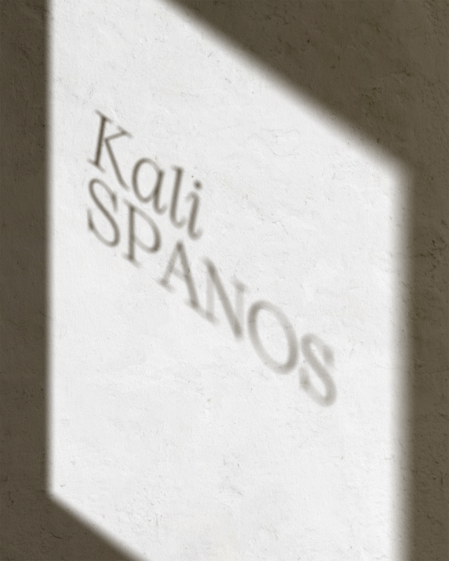 Shadow of the words 'Kali SPA' on a white textured wall, partially covered by a shadow.