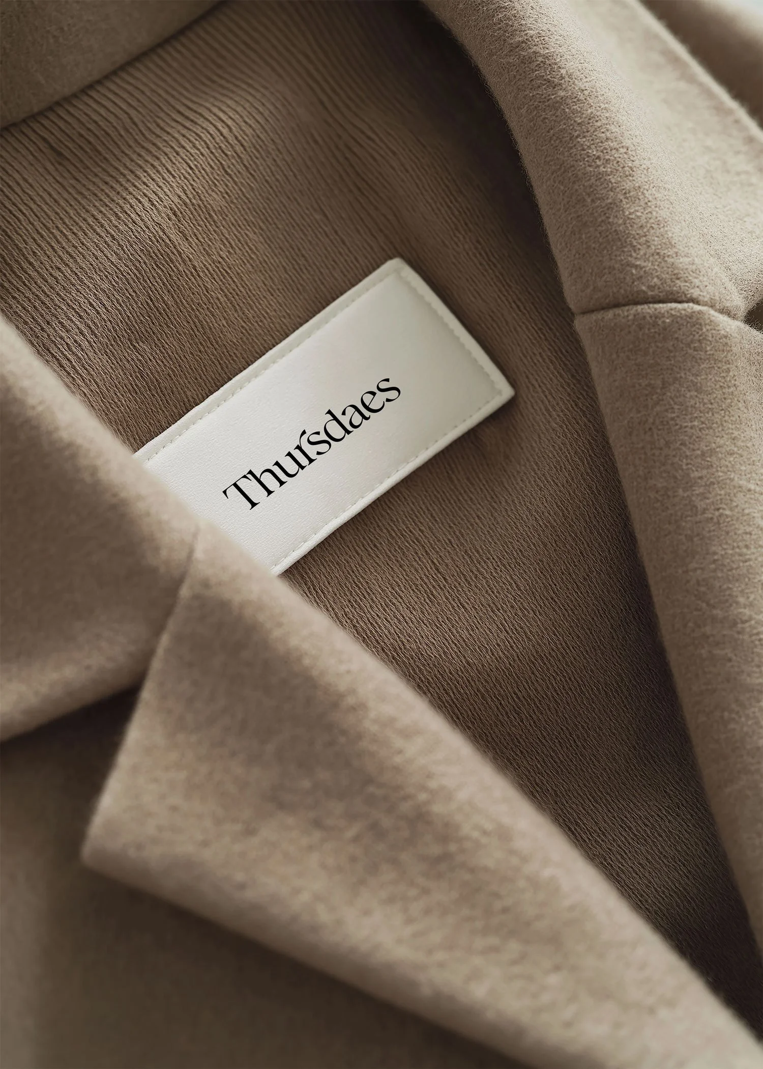 Close-up of a beige fabric interior with a white label reading 'Thursdaes' sewn into the lining.
