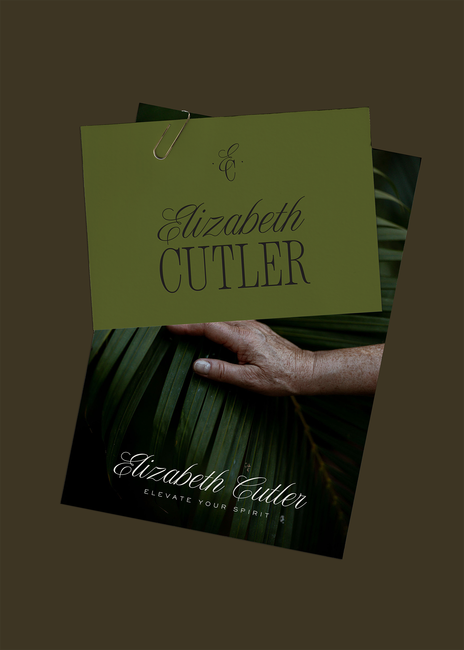 Close-up of two business cards for Elizabeth Cutler, one green with black text and the other black with white text, held together by a metal paperclip, against a blurry background of green palm leaves.