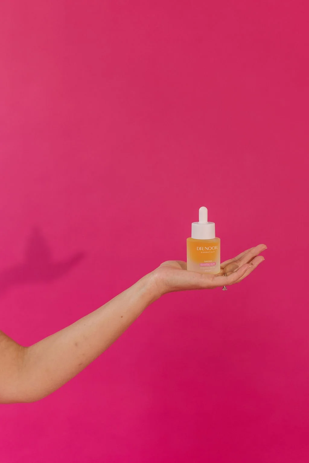 A hand holding a small yellow bottle with a white dropper cap against a pink background.