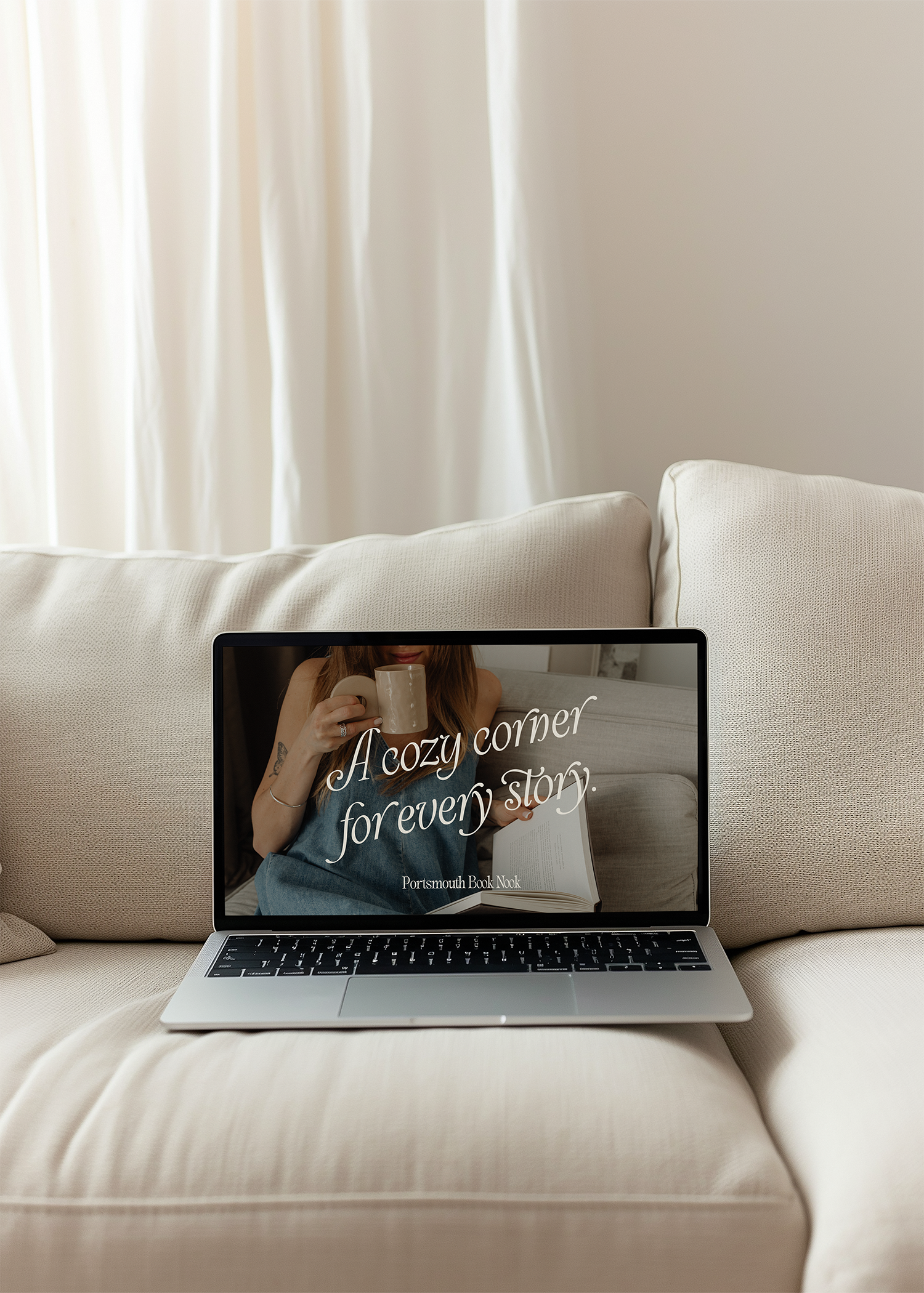 A laptop displaying the cover of a book titled 'A cozy corner for every story' by Portsmouth Book Nook, with a woman holding a mug and reading a book on the cover.