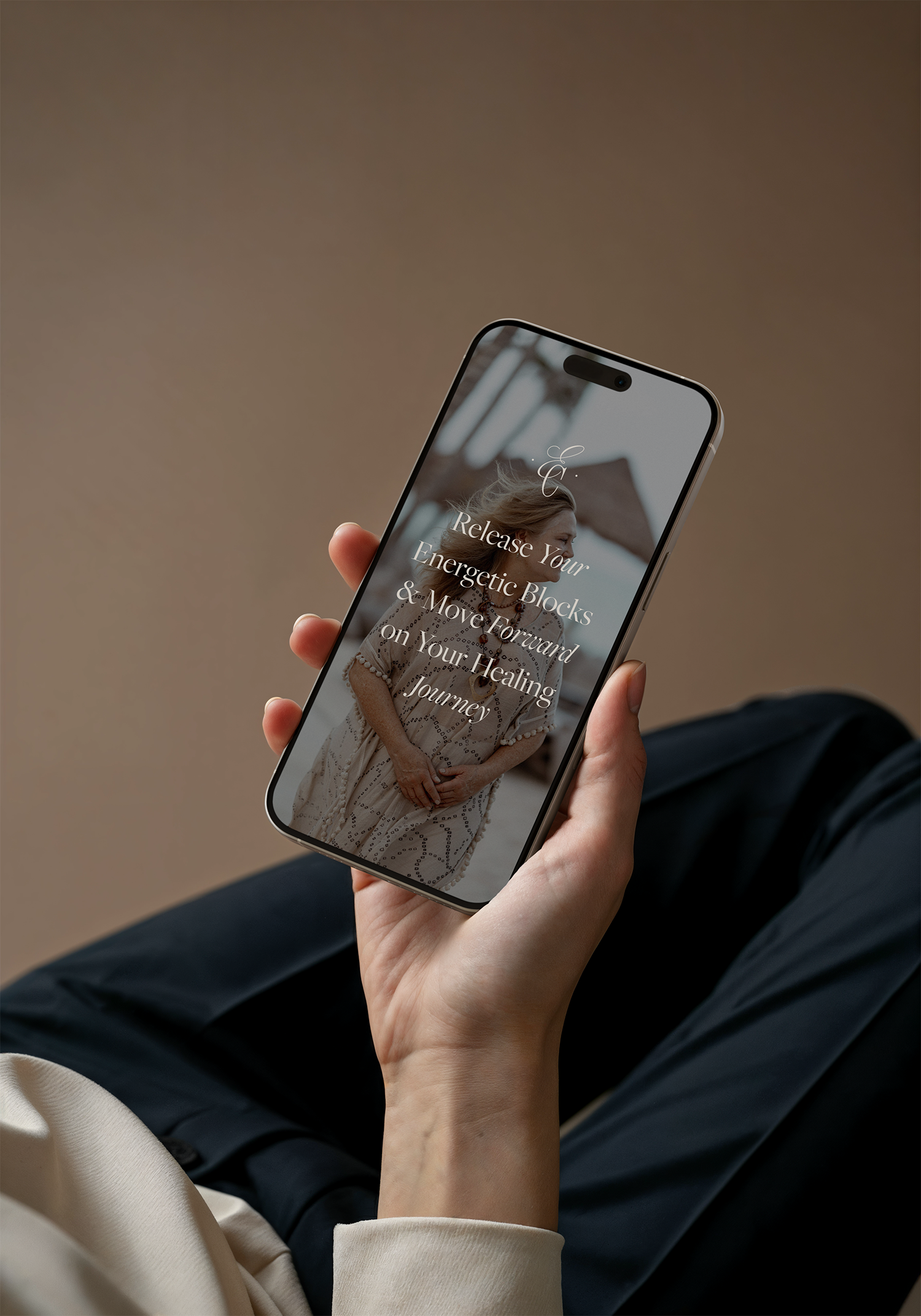 A person holding a smartphone displaying a webpage with a woman wearing bohemian clothing and jewelry, with text "Release Your Energetic Blocks & Move Forward on Your Healing Journey."