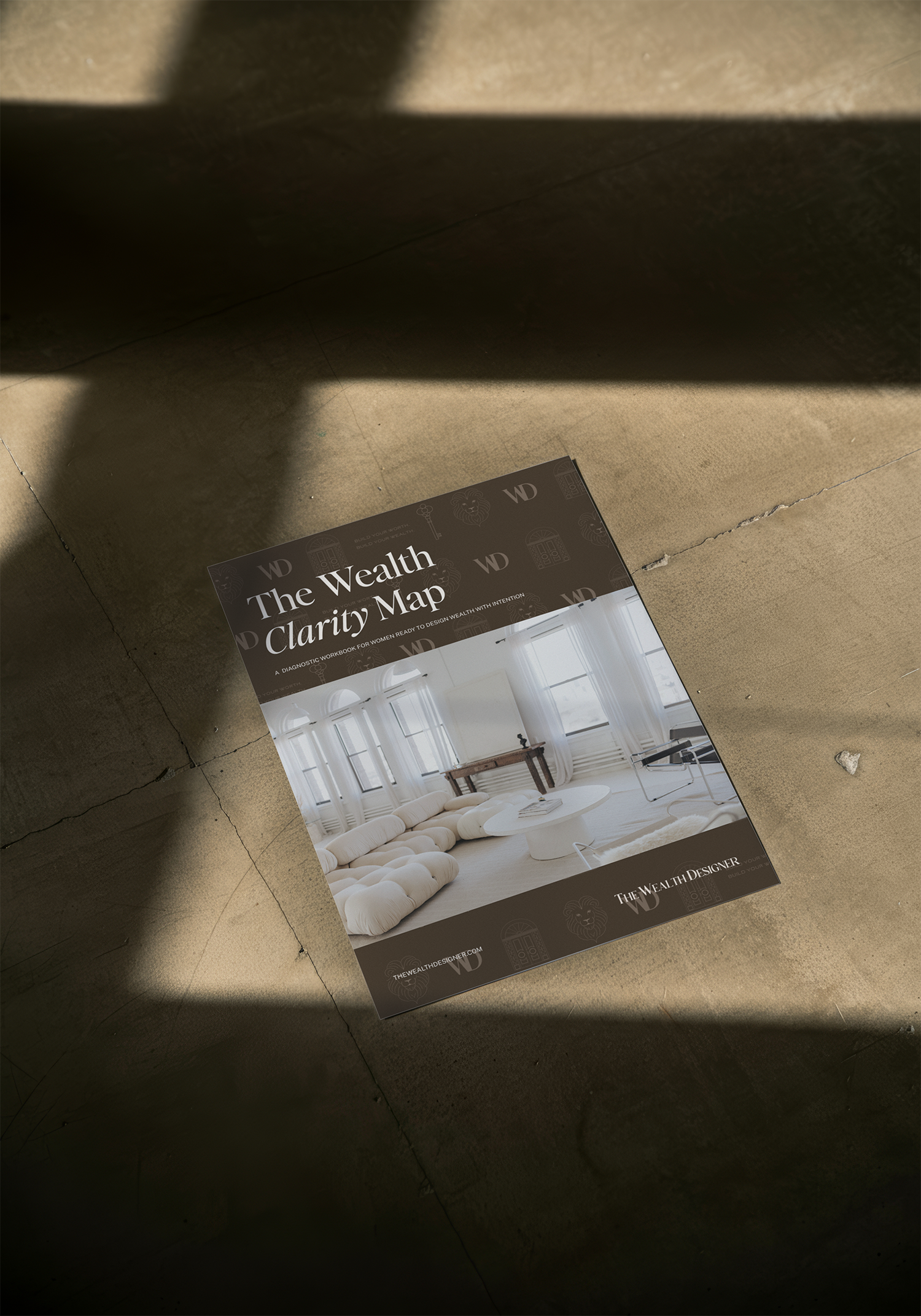 A magazine titled 'The Wealth Clarity Map' on a concrete floor, showing a bright, airy living room with white walls, large windows, a beige sofa, and a wooden table.