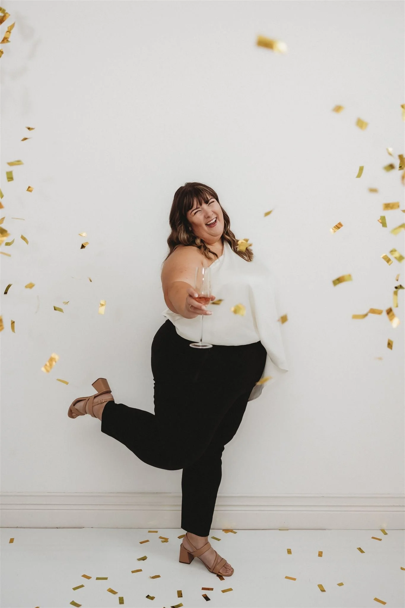 Systems expert, Bre Henderson, celebrating with gold confetti, holding a champagne glass, smiling, against a plain white wall.