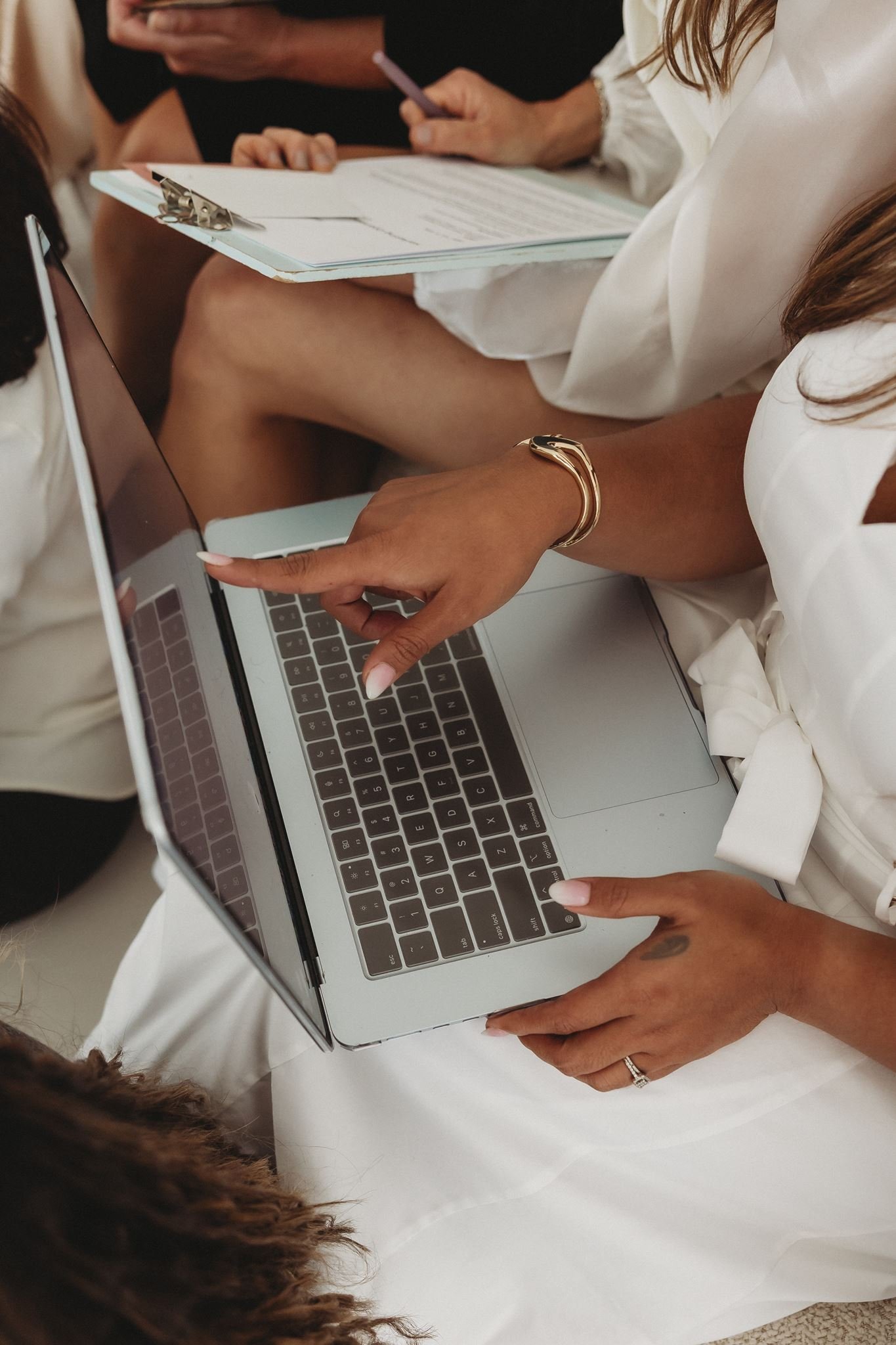 A person holding a smartphone displaying a feed from the Founding Females® women's business mastermind, with a laptop and a coffee cup on a white table in the background.