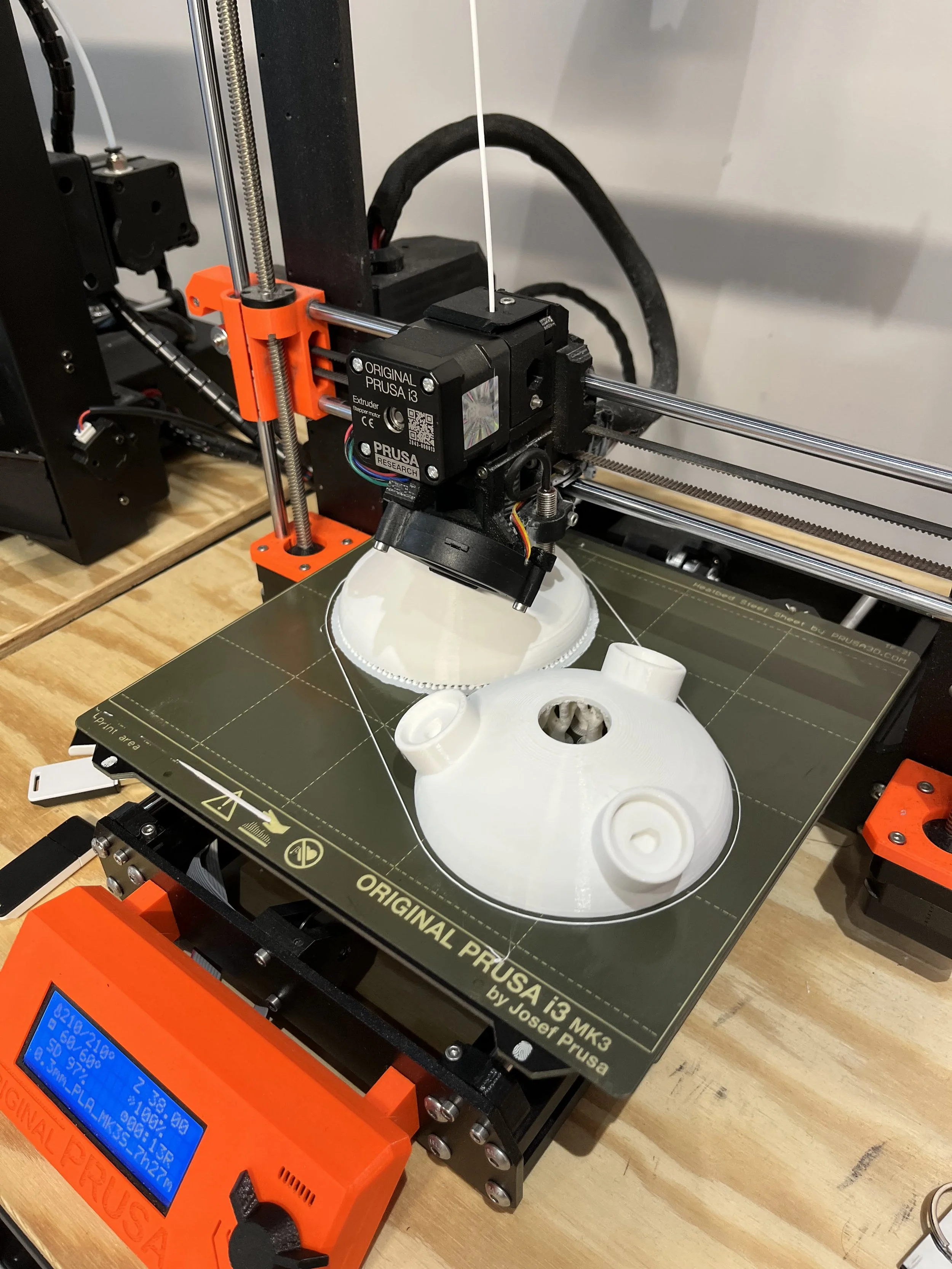 A 3D printer is creating a white model of the Millennium Falcon from Star Wars on a wooden work surface.