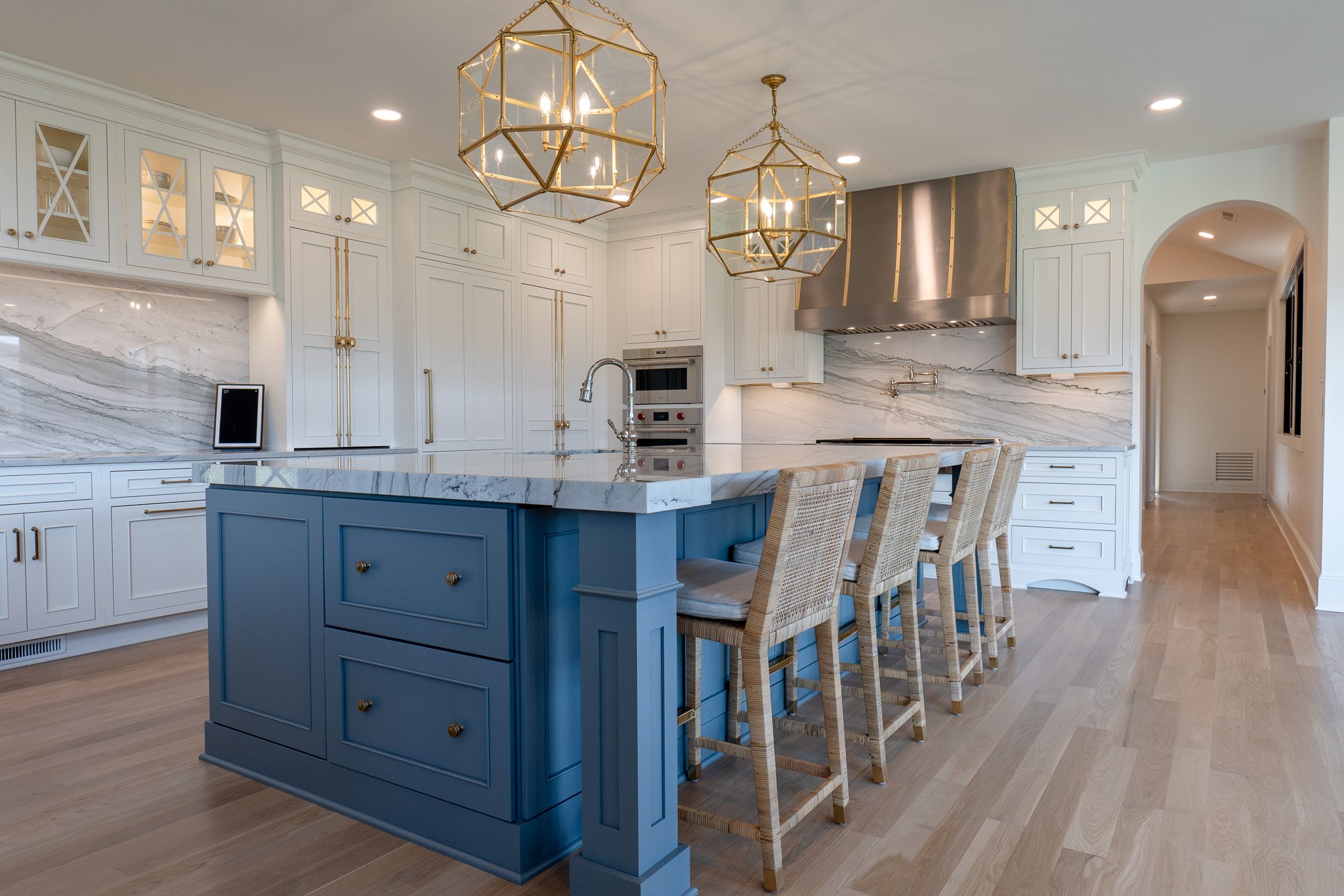 Modern kitchen with white cabinets, a blue island with marble countertop, four beige bar stools, and gold geometric pendant lights.