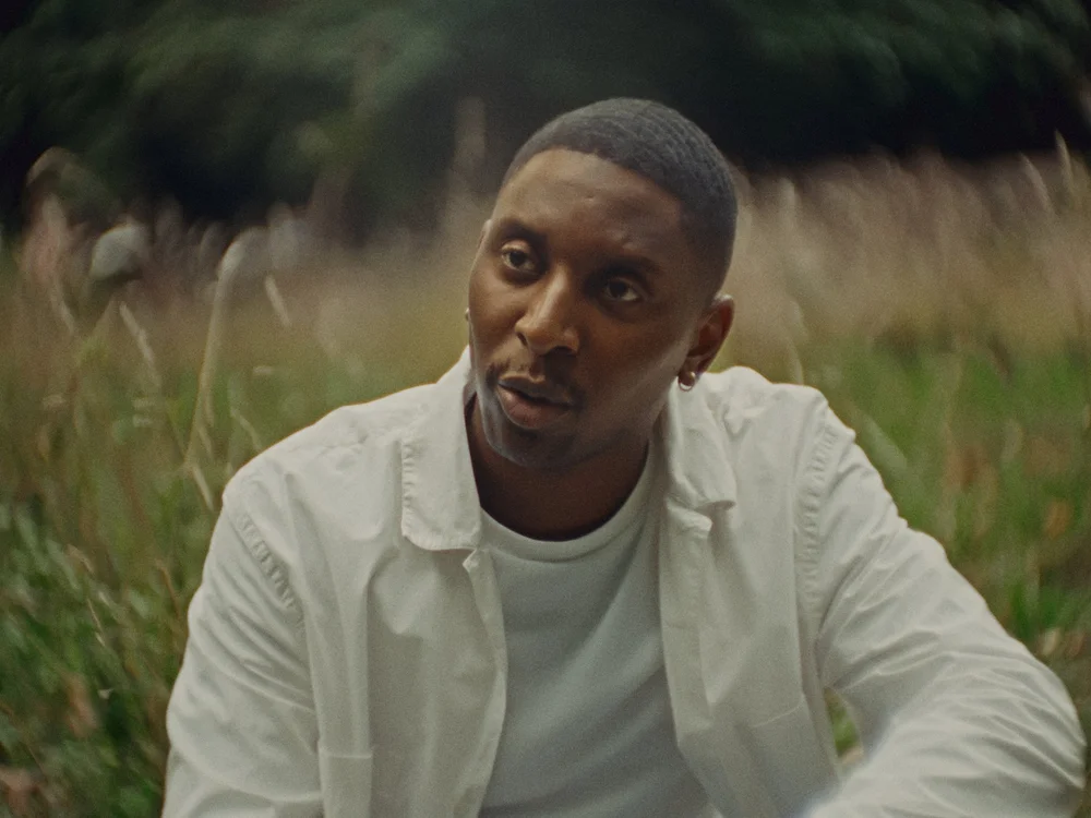 Samm Henshaw in a white shirt against soft woodland greens