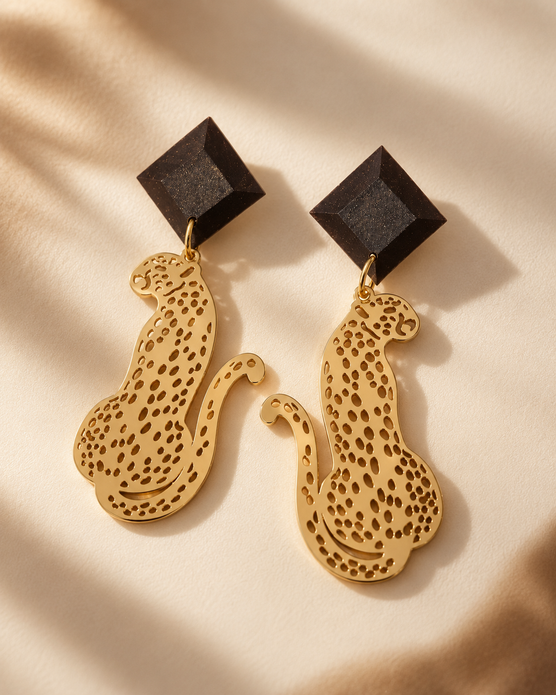 Model wearing Macula statement earrings with dark faceted coffee-stone studs and gold-plated leopard drops.