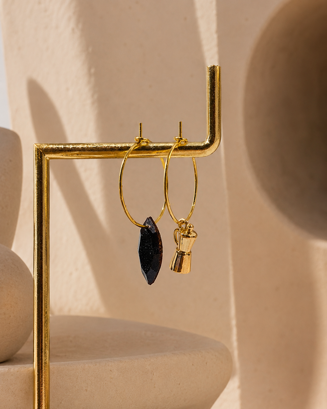 Grind earrings displayed on a gold stand, featuring 18K gold-plated coffee percolator charms and recycled coffee diamonds.