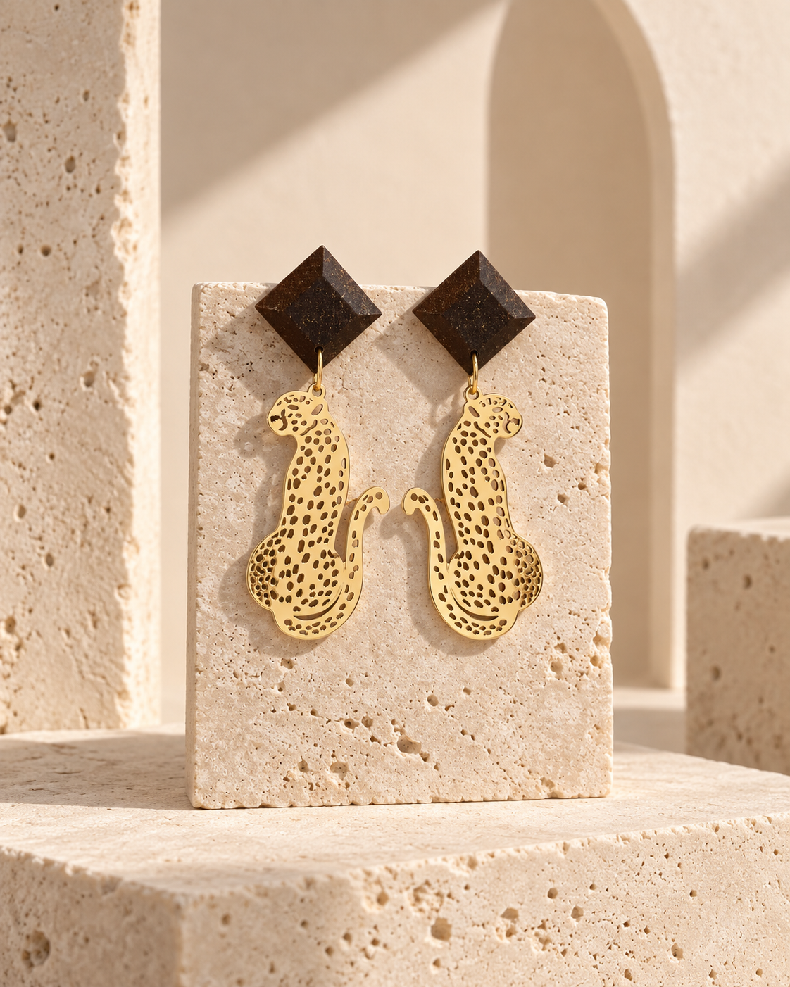 Macula leopard earrings with faceted coffee-stone studs and gold-plated leopard drops on a warm cream background.