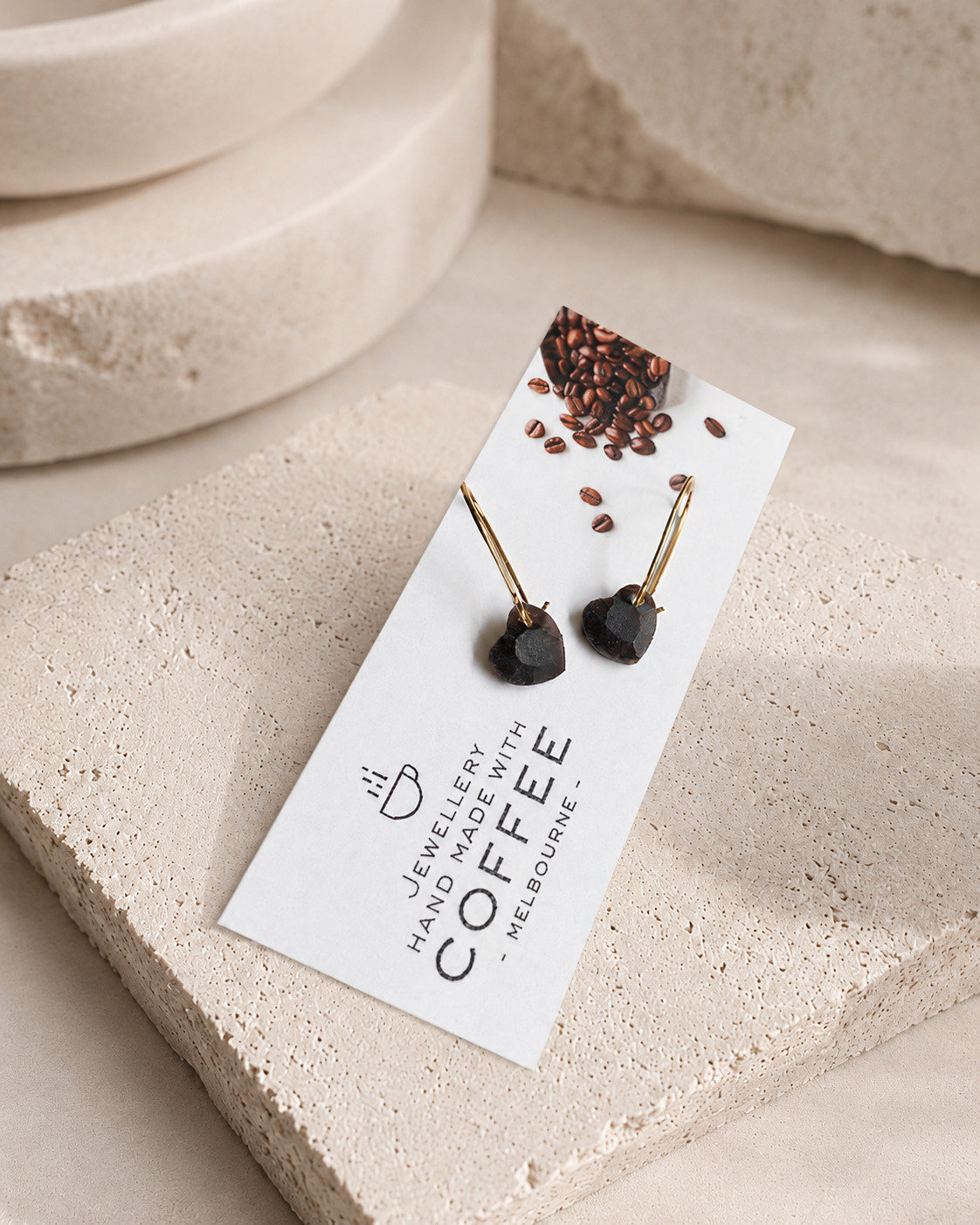 Faceted black heart earrings handmade from recycled coffee grounds and gold powder, styled on a soft stone display for Atelier Cayelle.