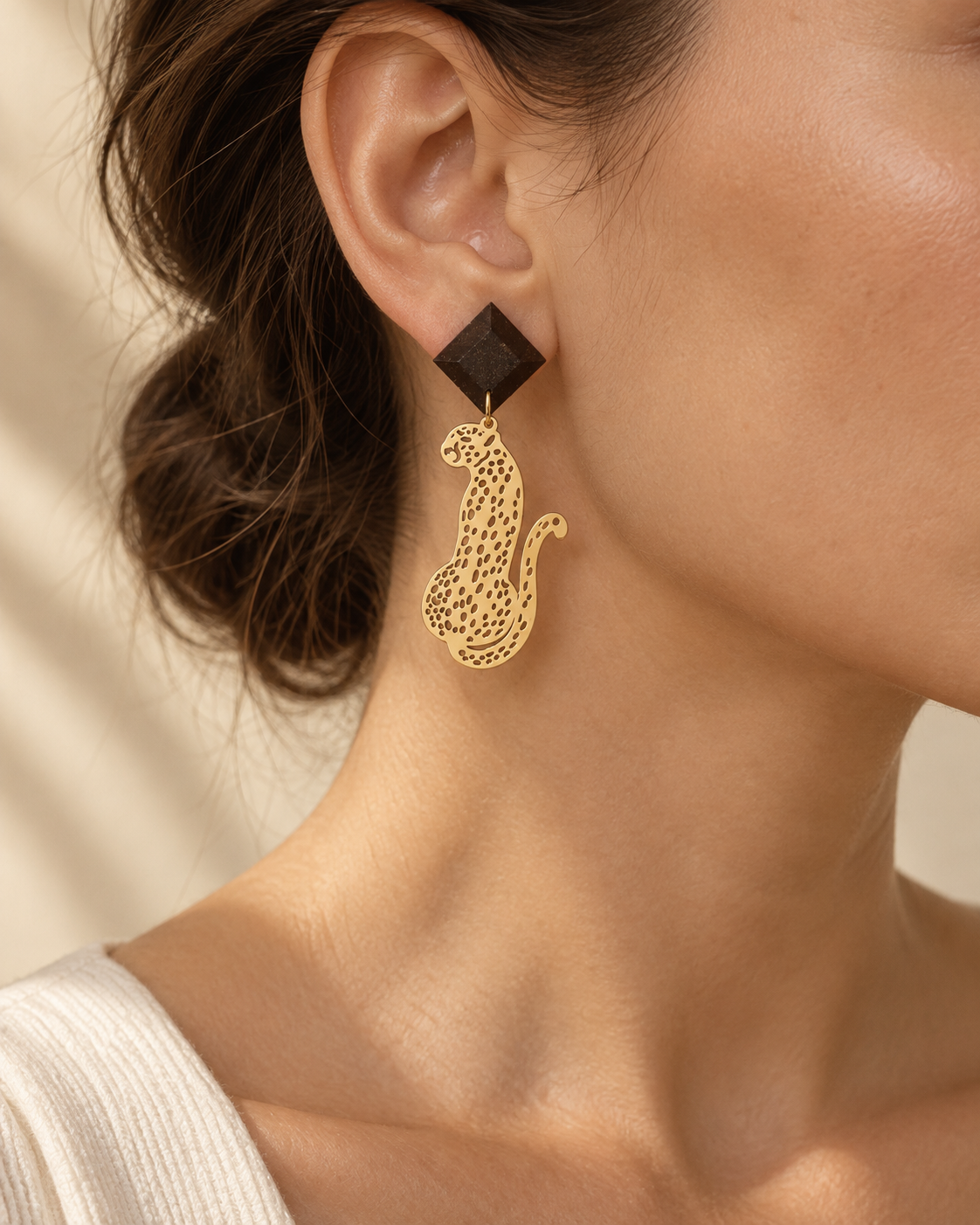 Close-up of Macula leopard earrings worn on the ear, showing the faceted coffee-stone stud and gold-plated leopard drop.