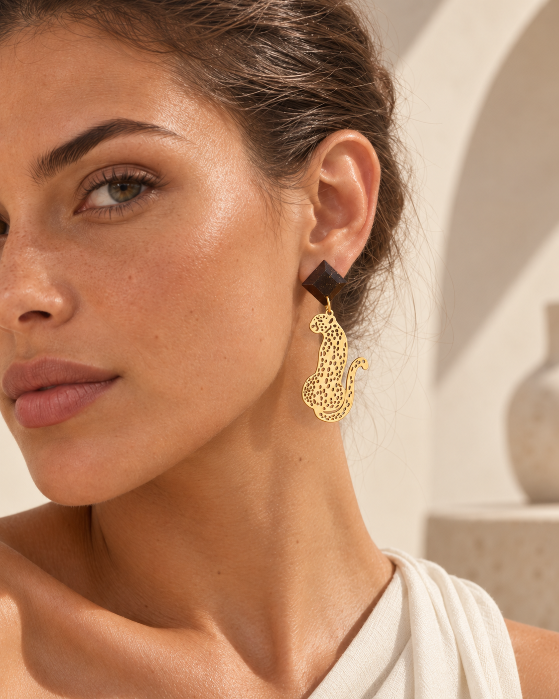 Macula coffee-stone and gold-plated leopard earrings displayed on a sculptural warm stone plinth.