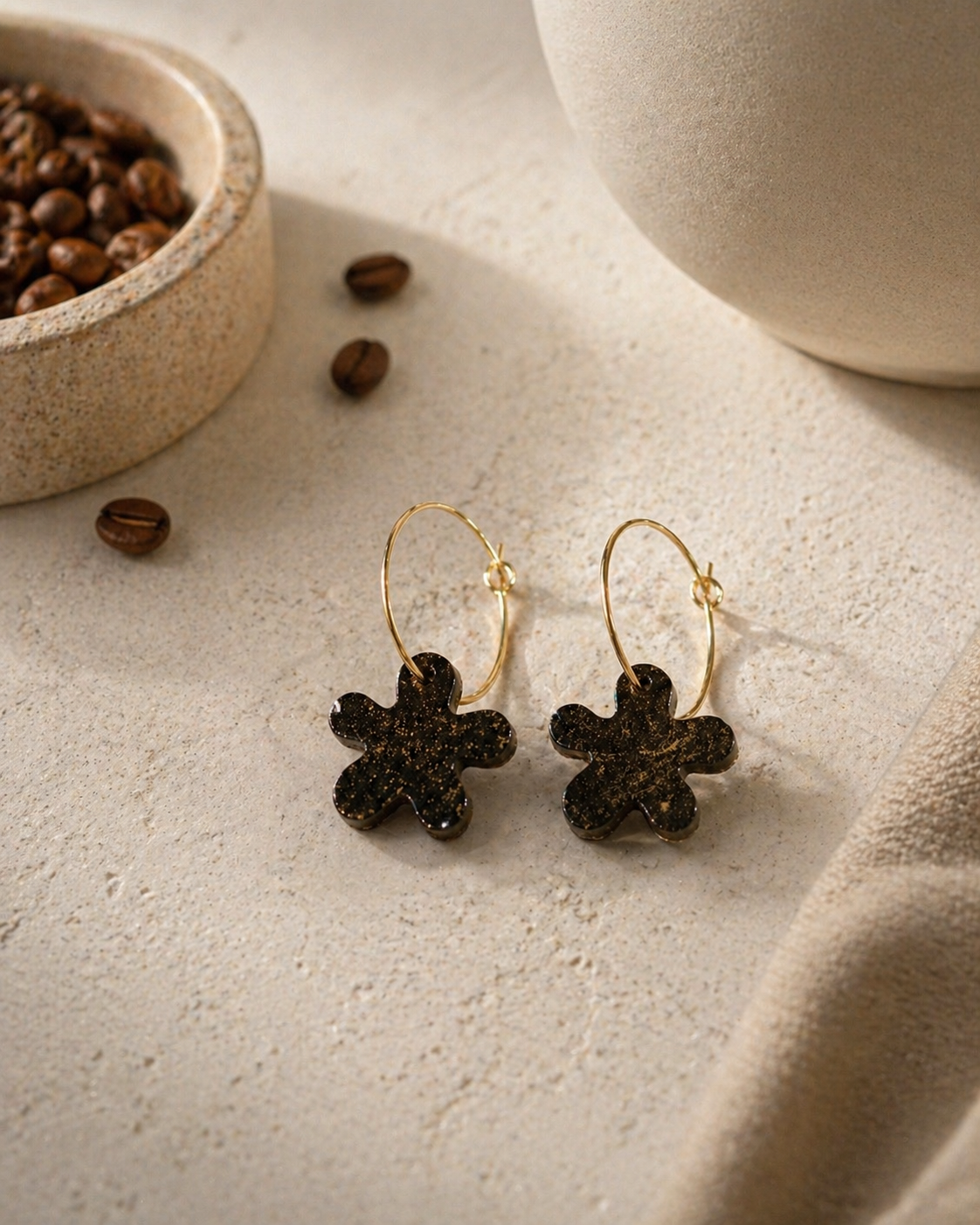 Black recycled coffee ground flower hoop earrings displayed with coffee beans on a neutral textured surface