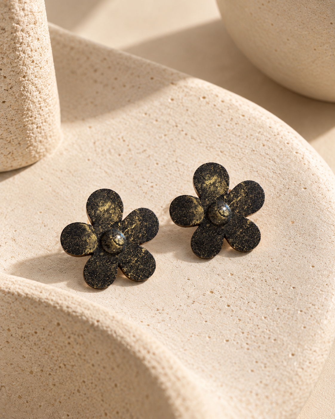 Nebula Bloom coffee-stone flower stud earrings with gold speckles displayed on a sculptural cream surface.