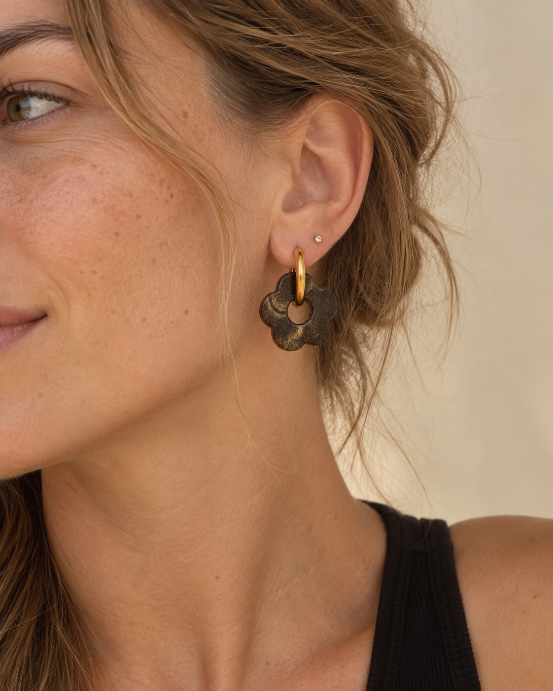Close-up of Liberica coffee-stone flower hoop earrings worn on the ear, showing the espresso-brown texture, gold details and scale.