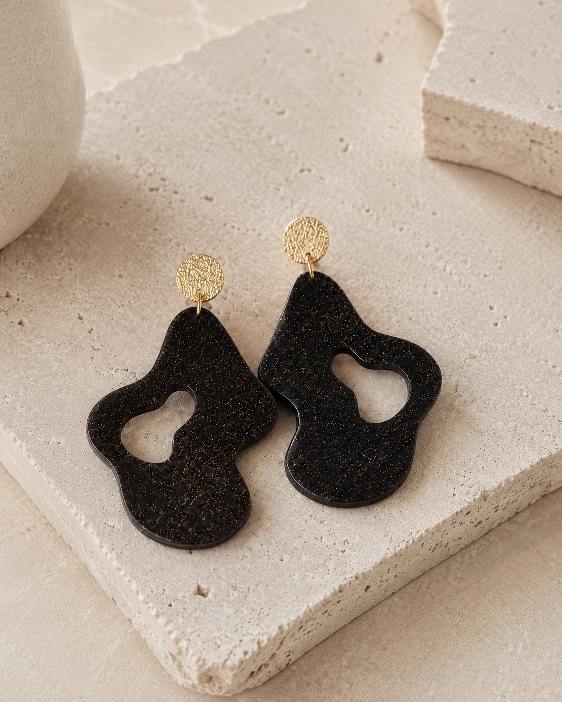 Jules recycled coffee statement earrings displayed on a textured stone surface, showing the organic black coffee-stone shape and 18K hammered gold-plated findings.