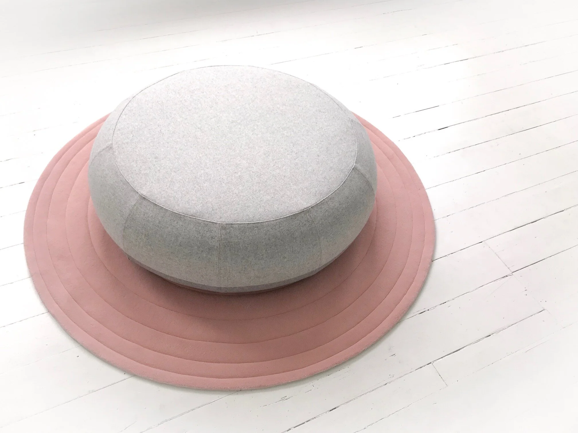 Round gray pouf on pink circular rug on white wooden floor
