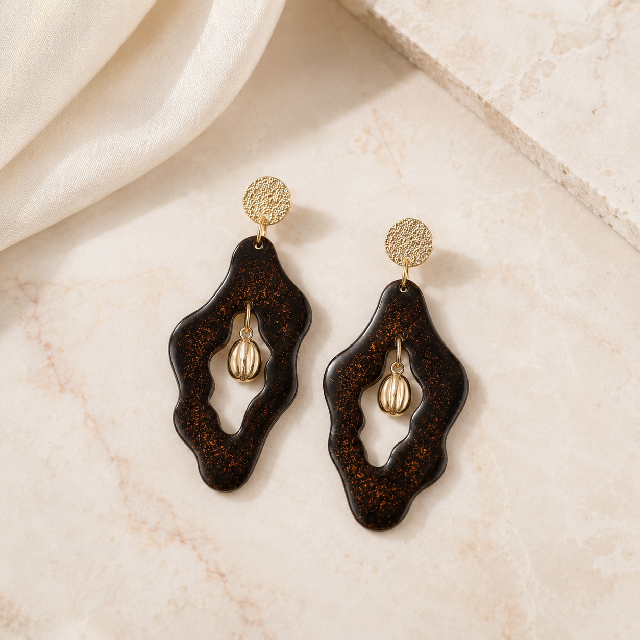 Oh My Bean handmade coffee ground earrings laid flat on textured stone, with real gold powder and gold-plated coffee bean centres.