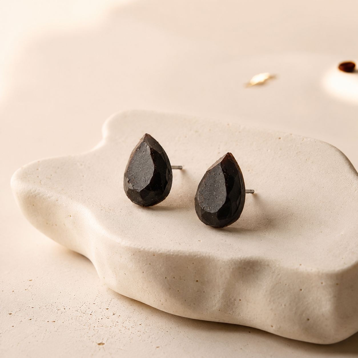 Drop recycled coffee-stone earrings from Atelier Cayelle with geometric teardrop shapes on a warm ceramic dish.